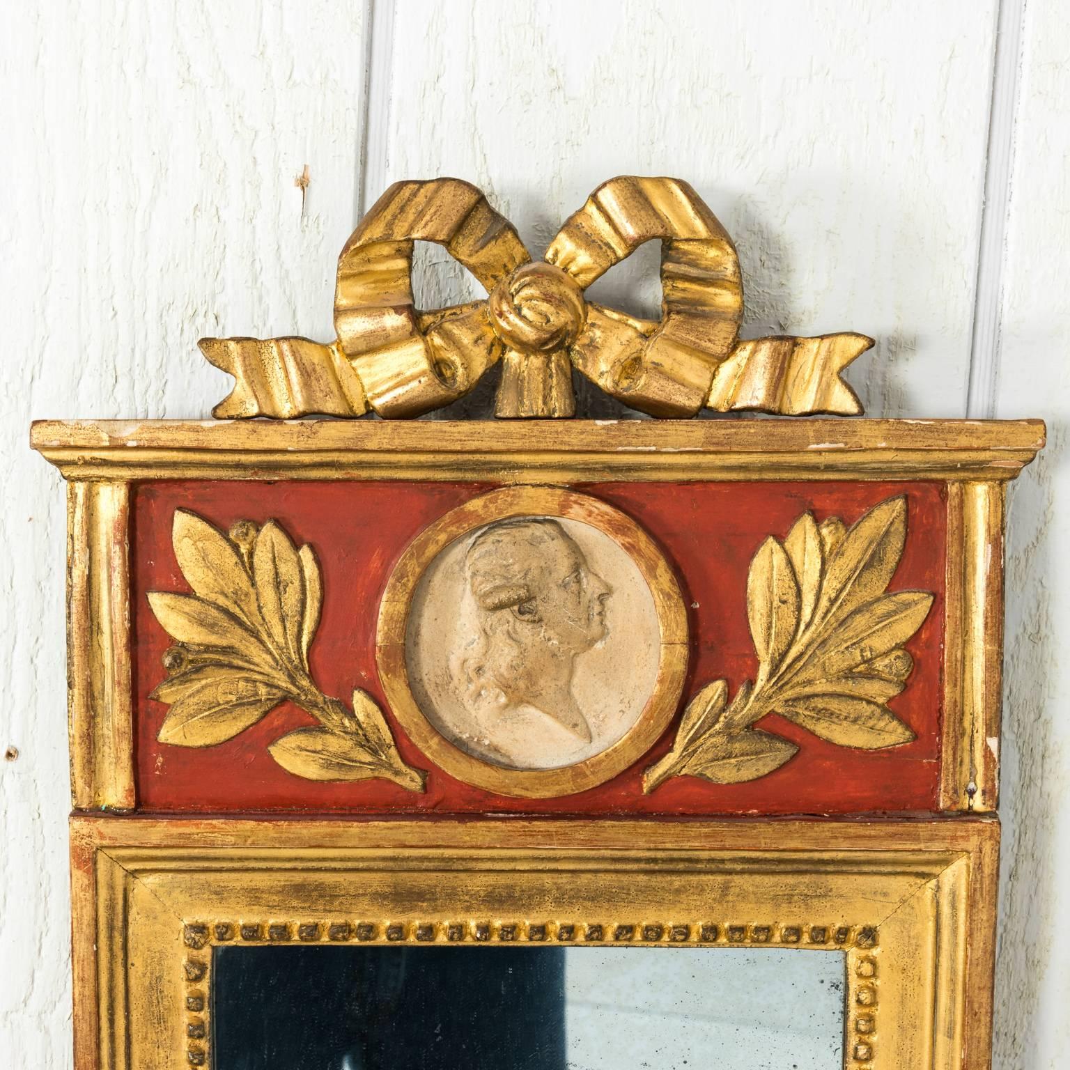 A gilt and red-painted late-Gustavian mirror with carved ribbon crest decor.
 