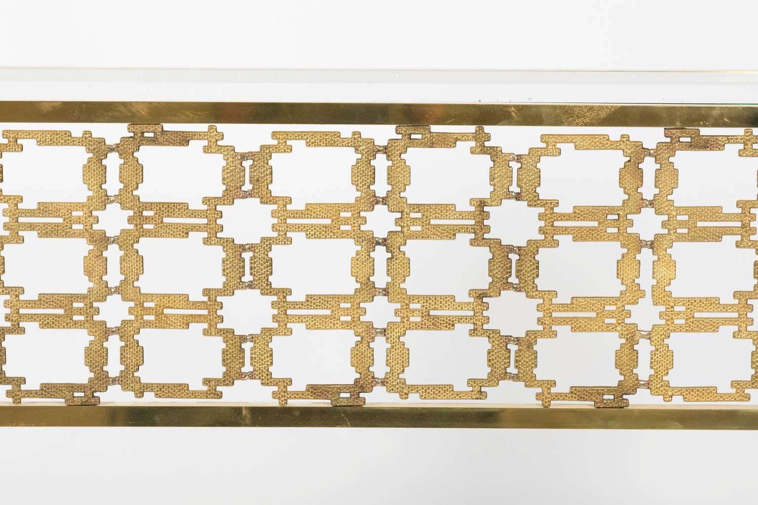 Pair of brass console tables that feature a pierced geometric skirt and glass top, circa mid-20th century.