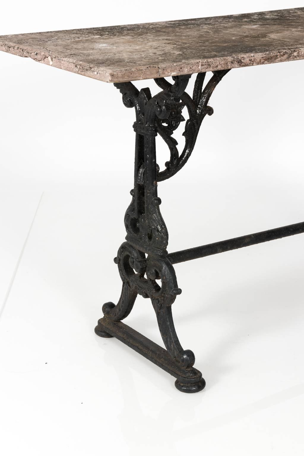 Late 19th century cast iron base baker's table featuring floral and scroll motif with a stretcher. Marble has unfinished rough finish with patina due to the process of oxidation.