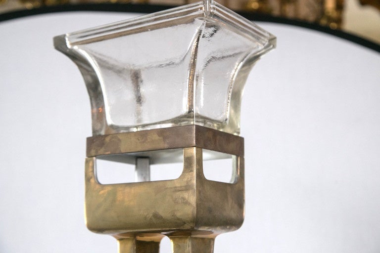 Topped by a thick glass "shade" this torchiere throw light upwards from the socket found just below the glass in the top of the brass housing.
Double legs in a rectangular base. Step on switch is part of the power cord. Width 12 inches,