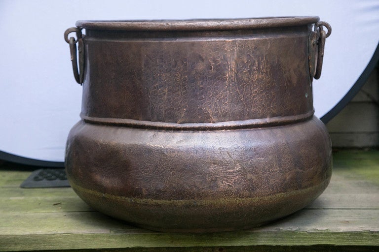 A beautifully made copper vessel or vat, hand-hammered, with two hanging wrought iron handles. Perfect for kindling or logs. Visible dent can probably be banged out. Diameter at widest part is 24 inches (approx.) rolled rim, two patches done in