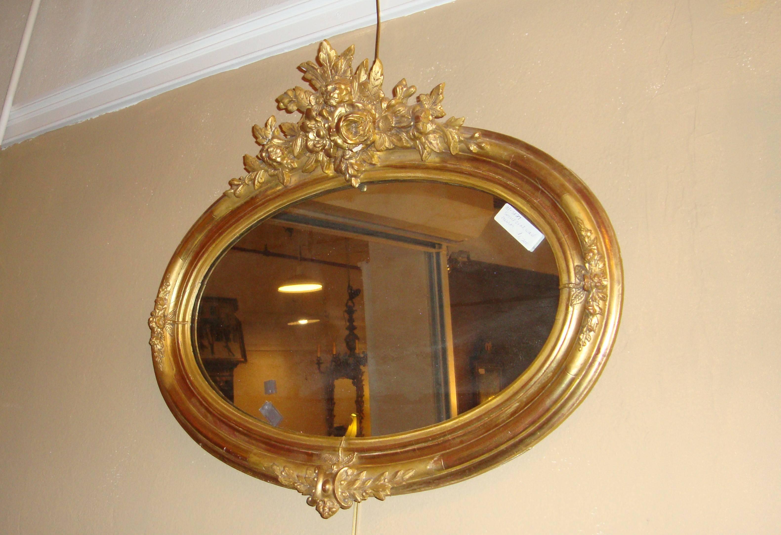 A small Louis XVI style oval wall mirror, with gilt and floral accents.