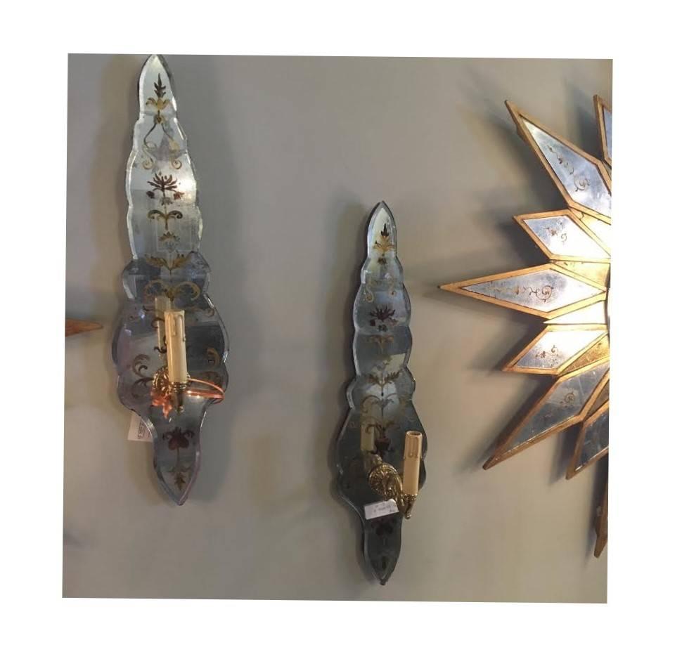 Pair of églomisé sconces, with a single arm by Maison Jansen. Each mirrored panel is beveled with gilt floral and rose design of églomisé quality. Both hold a single electrified bronze sconce.