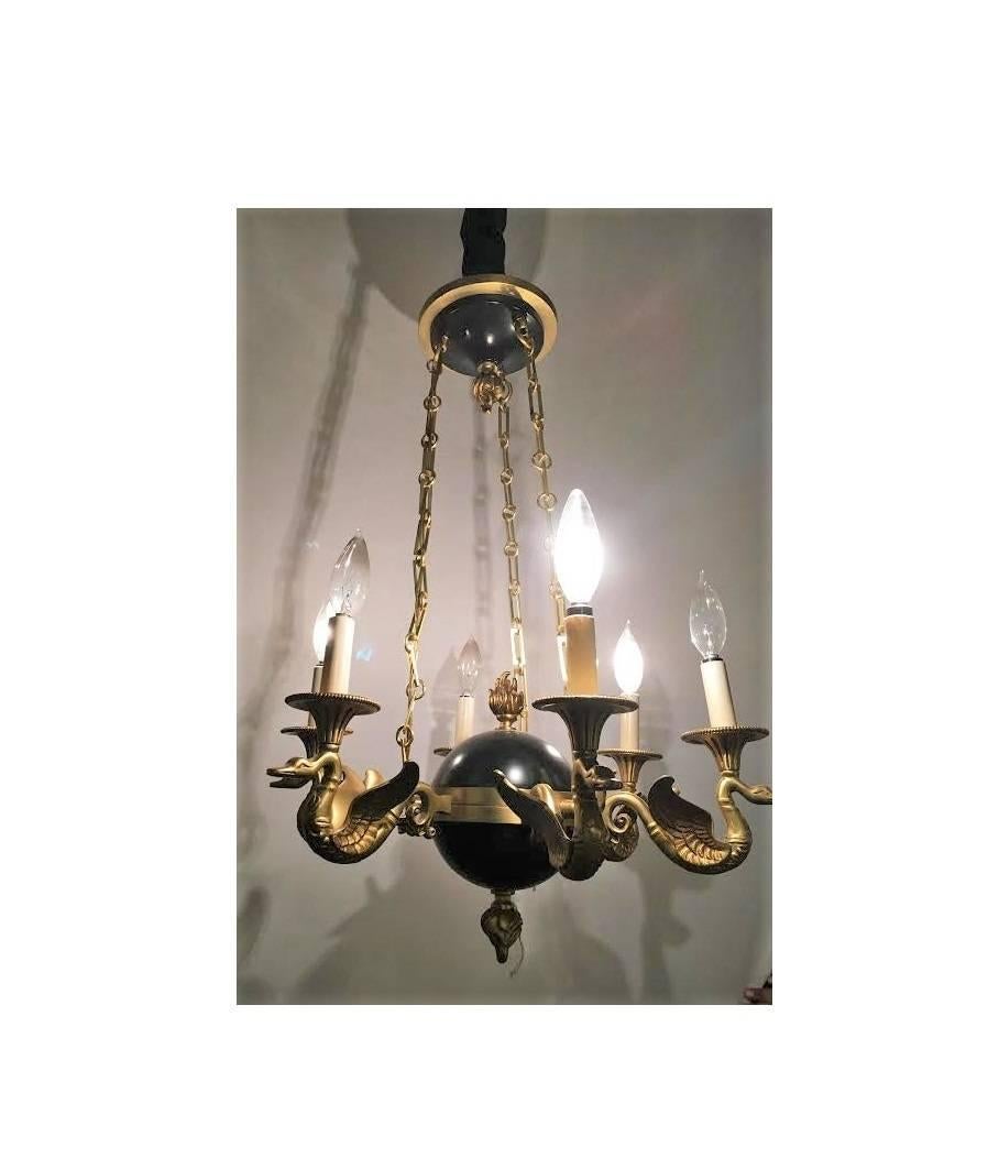 A regency style six-arm bronze swan decorated chandelier. This six-arm chandelier depicting swans chained to a centre ball decorated with a ebony finish. The whole supported by a set of three chains imprisoning the swans to a cap with a bronze flame