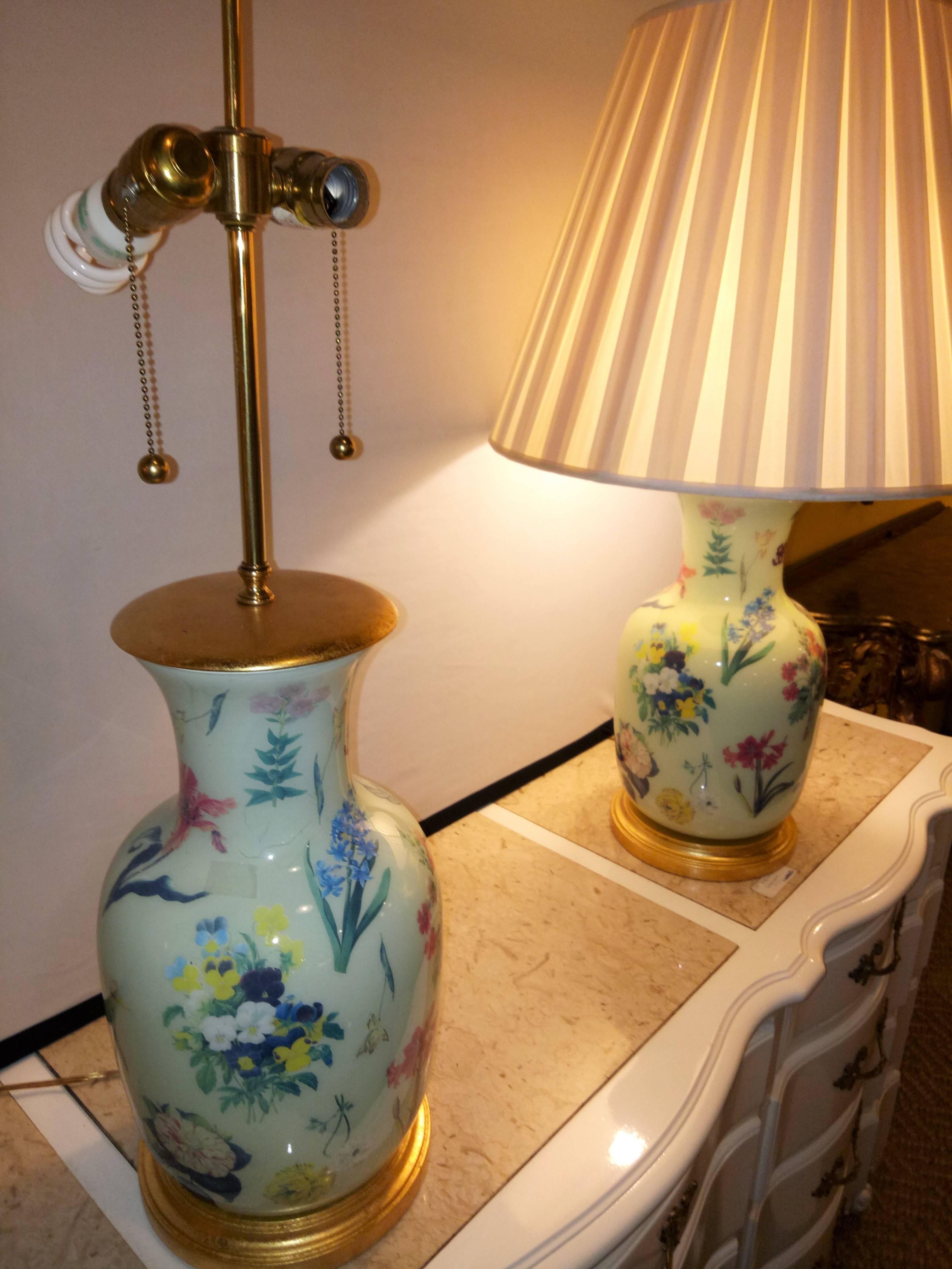 Pair of porcelain hand-painted ginger jar lamps. The pair of lamps are an off-white color with a golden top as well as base, and have a beautiful floral print throughout. It requires two bulbs ( 275W). These have custom shades that are 15 inches