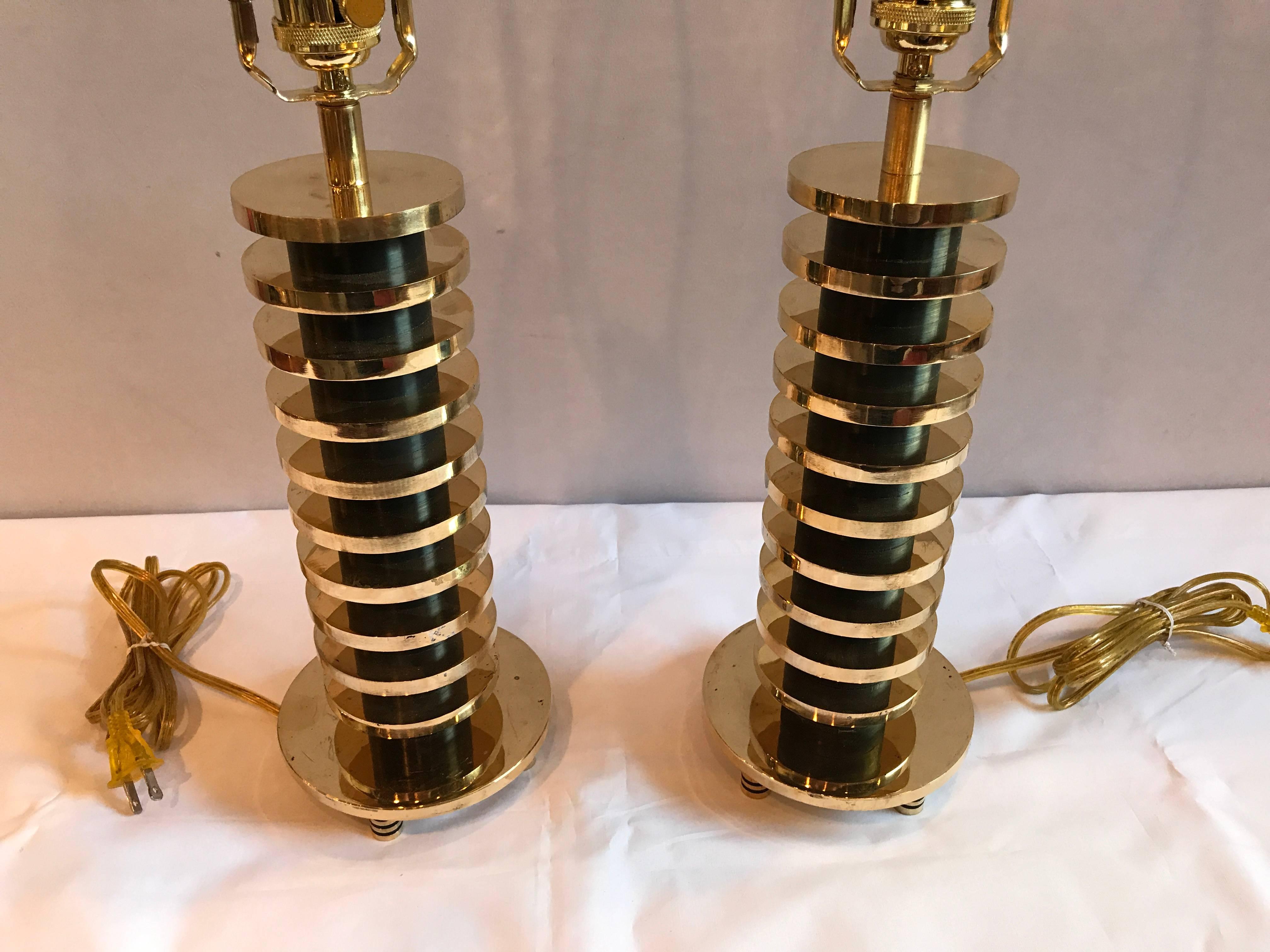 A pair of brass and metal disk shaped Mid-Century Modern table lamps. This listing is for one of three sets of brass disk form table lamps. The newly wired lamps come without shades. Having an ebony tube shaped centre column with a group of brass