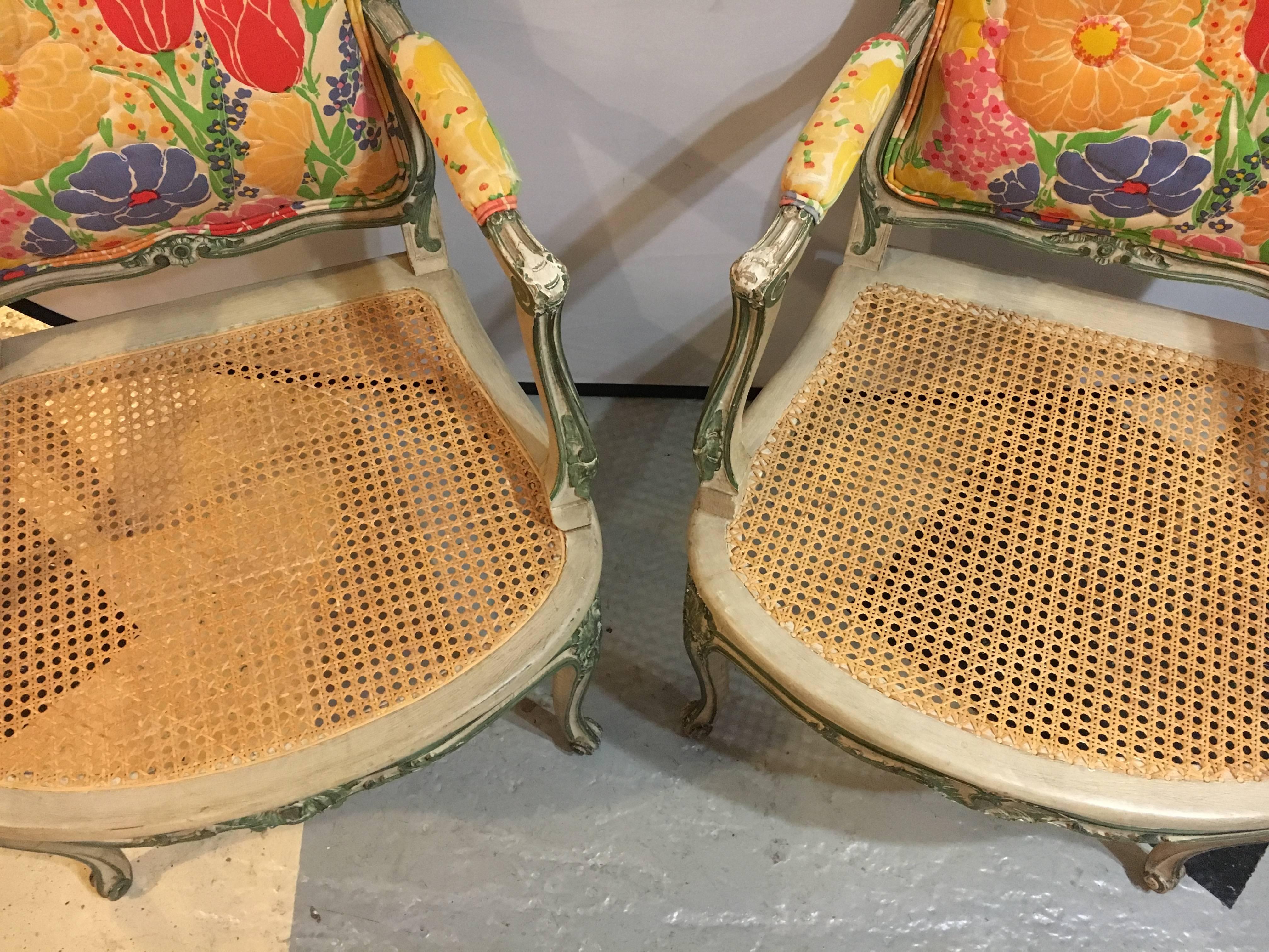 Pair of Louis XV style Hollywood Regency poly-chrome decorated fauteuils. This fine pair of attributed Jansen armchairs have cane seats which support stuffed colorful floral decorated cushions and backrests. Perfect for any Florida or sun-room.