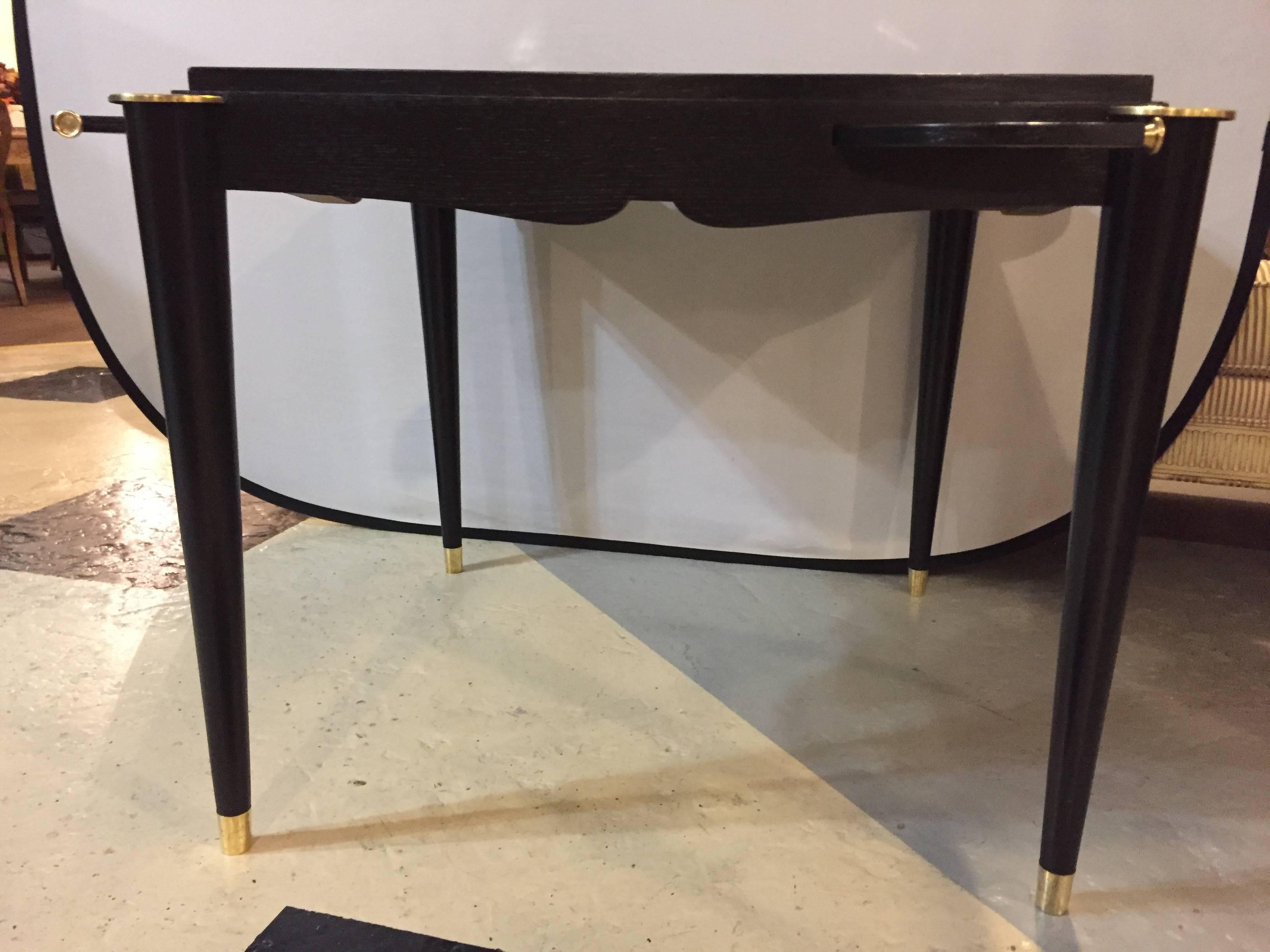An ebonized Mid-Century Modern card or game table with reversible top and four brass pull-out coin trays. The fine tapering legs having bronze sabots and terminate in very decorative bronze circular corners leading to a tabletop that shows a fine
