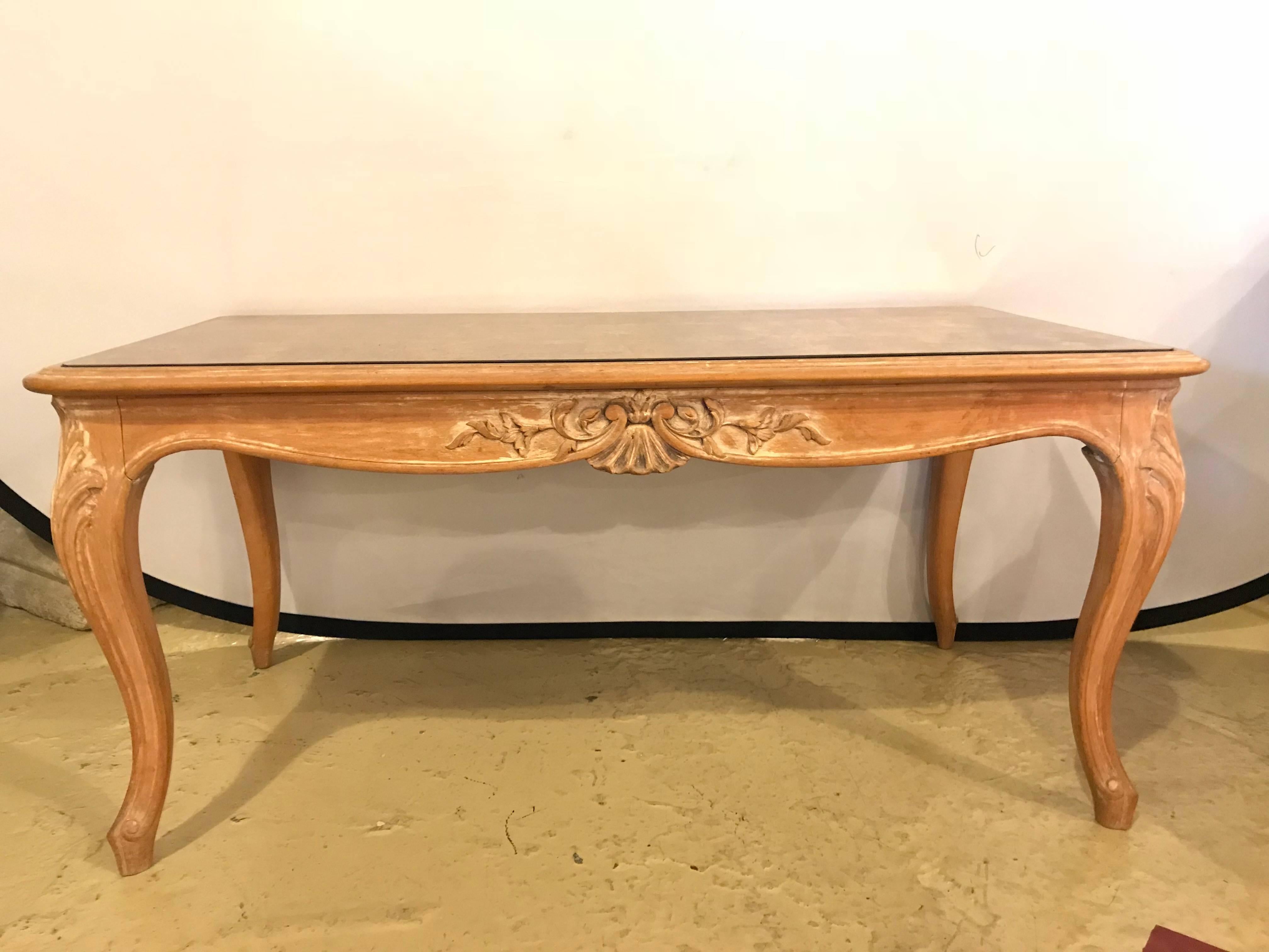 A Louis XV style white washed coffee table with decorated gilt gold glass top. Hollywood Regency at its finest. This wonderfully carved and detailed coffee or low table is simply stunning and is certain to shine in most any home.