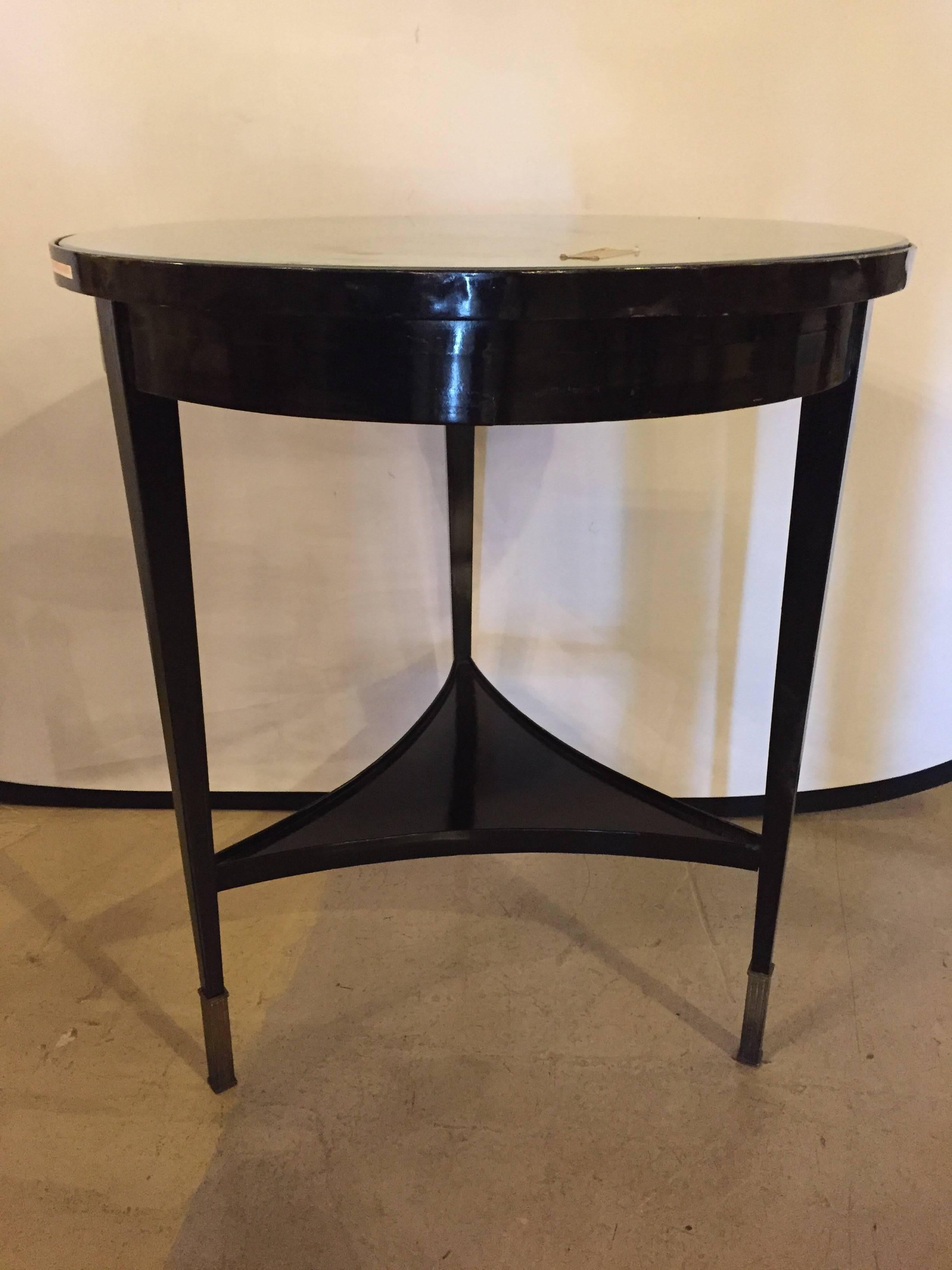 An ebonized silver gilt mirror top centre or end table. On bronze sabots having tapering legs with a lower triangular inverted shelf this sleek and stylish end table is certain to add that Hollywood Regency charm that is highly sought after.