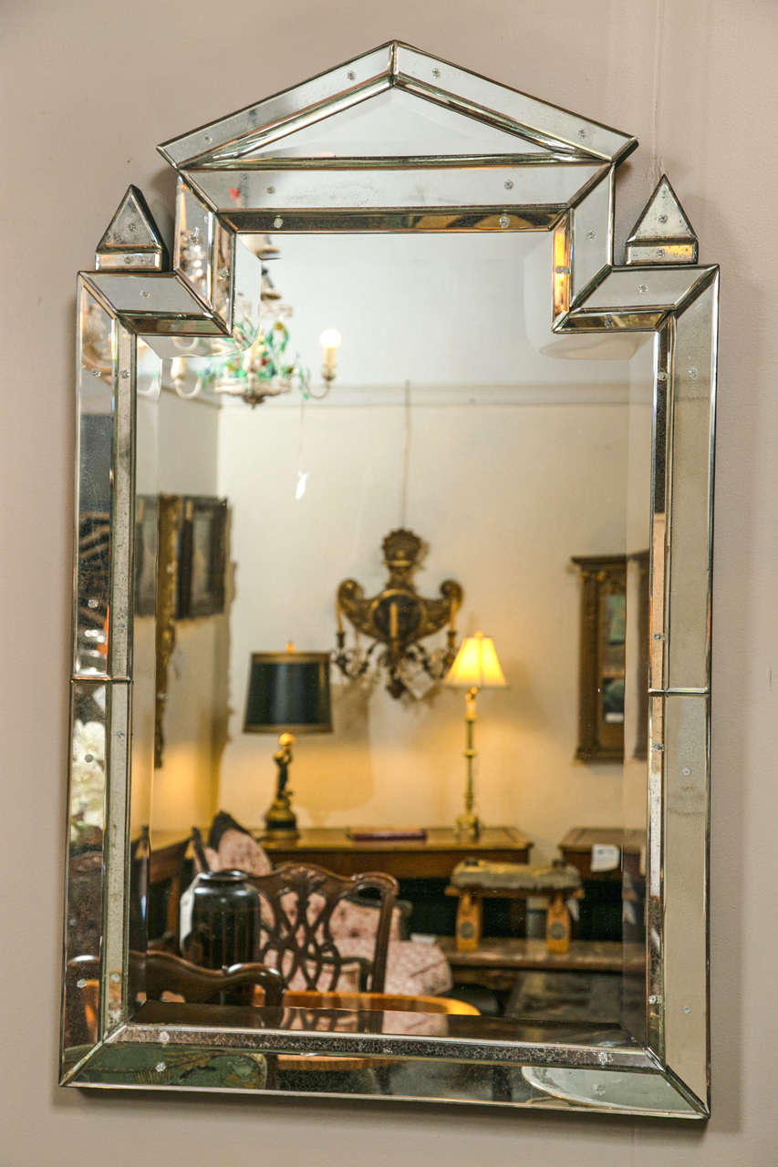 Pair of Piedmont Hollywood Regency style mirrors. The central beveled mirror framed in an all-over distressed antiqued beveled mirror border. The bottom of rectangular design leading to a triangular top flanked by mirrored finials. We have a pair of