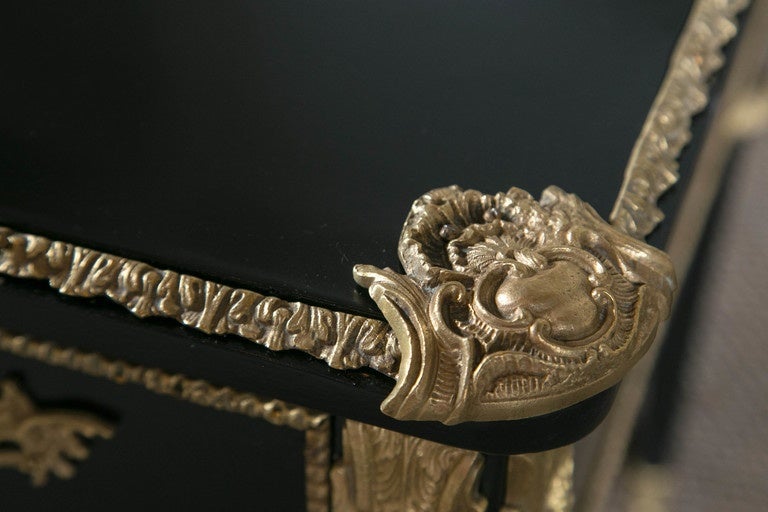 A Maison Jansen bronze-mounted and ebonized desk. This heavily bronze-mounted Louis XVI style desk by Jansen has bronze chased sabots leading to tapering legs terminating in bronze capitals. The case having a knee hole center with a center drawer