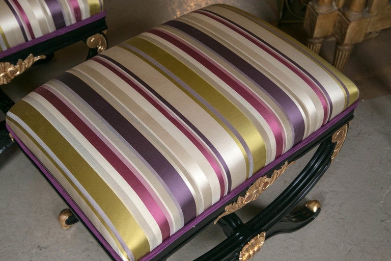 Pair of Maison Jansen style X benches. Ebonized with gilt gold accents, fantastic fabric and comfort galore. One of a kind color scheme that adds a Hollywood Regency modernistic vibe - golden sun, ivory, beach gray, violet and purple sage screams