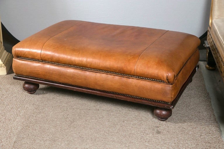 Ralph Lauren leather ottoman or footstool. Supported by bun feet and a solid wooden apron this leather ottoman is almost sofa bed in size and has the signature Ralph Lauren distressed leather look along with nail tacks throughout.
