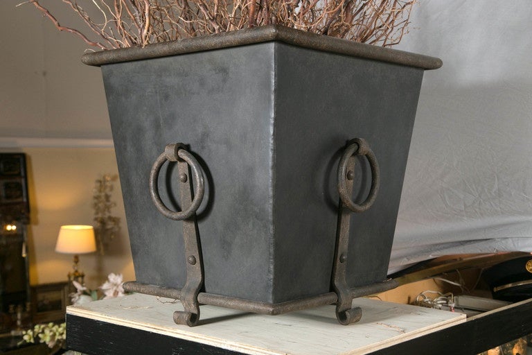 Pair of vintage monumental wrought iron decorative planters/Jardinieres. Each with soldered solid supports leading to circular handles. The cylindrical apron supporting an inverted tapering square form case terminating in a cylindrical top. This
