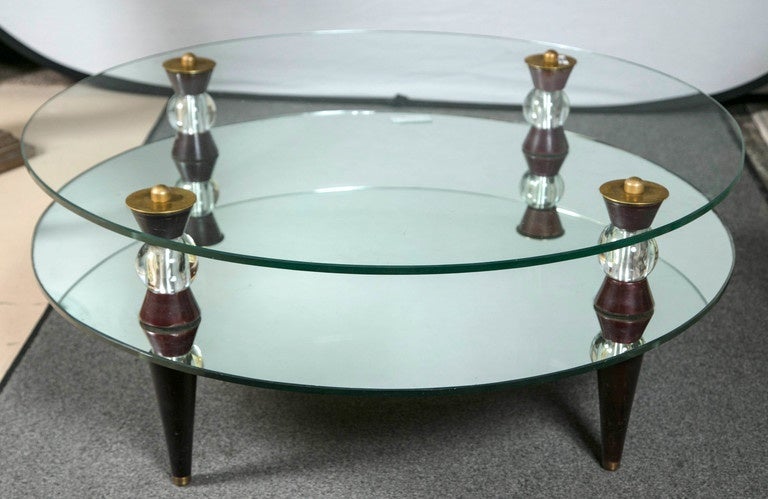 A fine Art Deco style glass and mirrored Mid-Century Modern coffee table. This decorative coffee has a pair of end tables that match and are sold separately. Each have mahogany tapering legs leading to a bottom circular mirrored glass shelf which