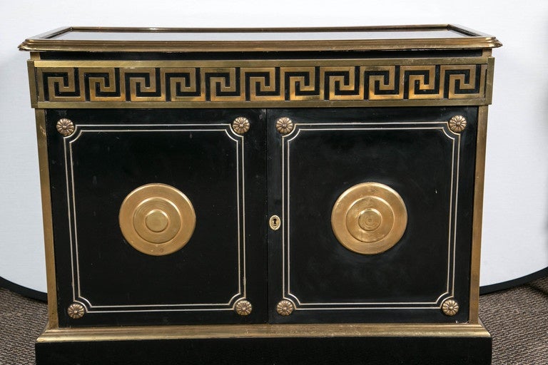 Style and flair abound with this finely constructed vintage ebonized Greek key design commode. Hollywood Regency at its absolute finest. The bracket base leading to a bronze framed CAP supporting a pair of heavy bronze mounted doors each with double