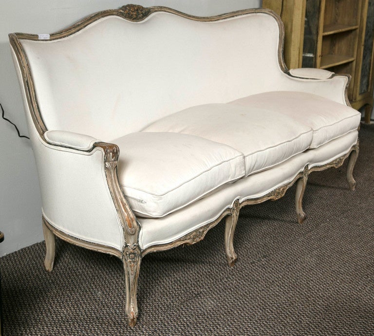 Louis XV style distressed paint sofa attributed to Maison Jansen. This three-seat down feather cushion sofa sits on a finely distressed frame. The cream color with blue green detailed hi lights. The frame with all around rosette carvings as well as