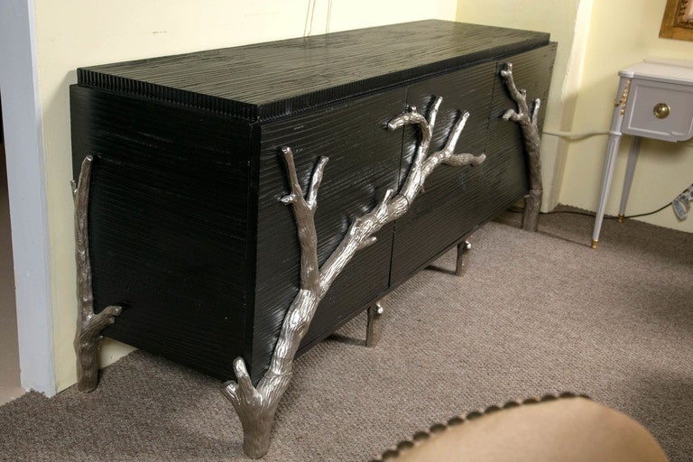 A Hollywood Regency style ebonized sideboard with silver gilt metal drawer pulls. This finely ebonized sideboard has three doors leading to a shelf open interior. The front and side with metal silver branch decorated design sitting on silver metal