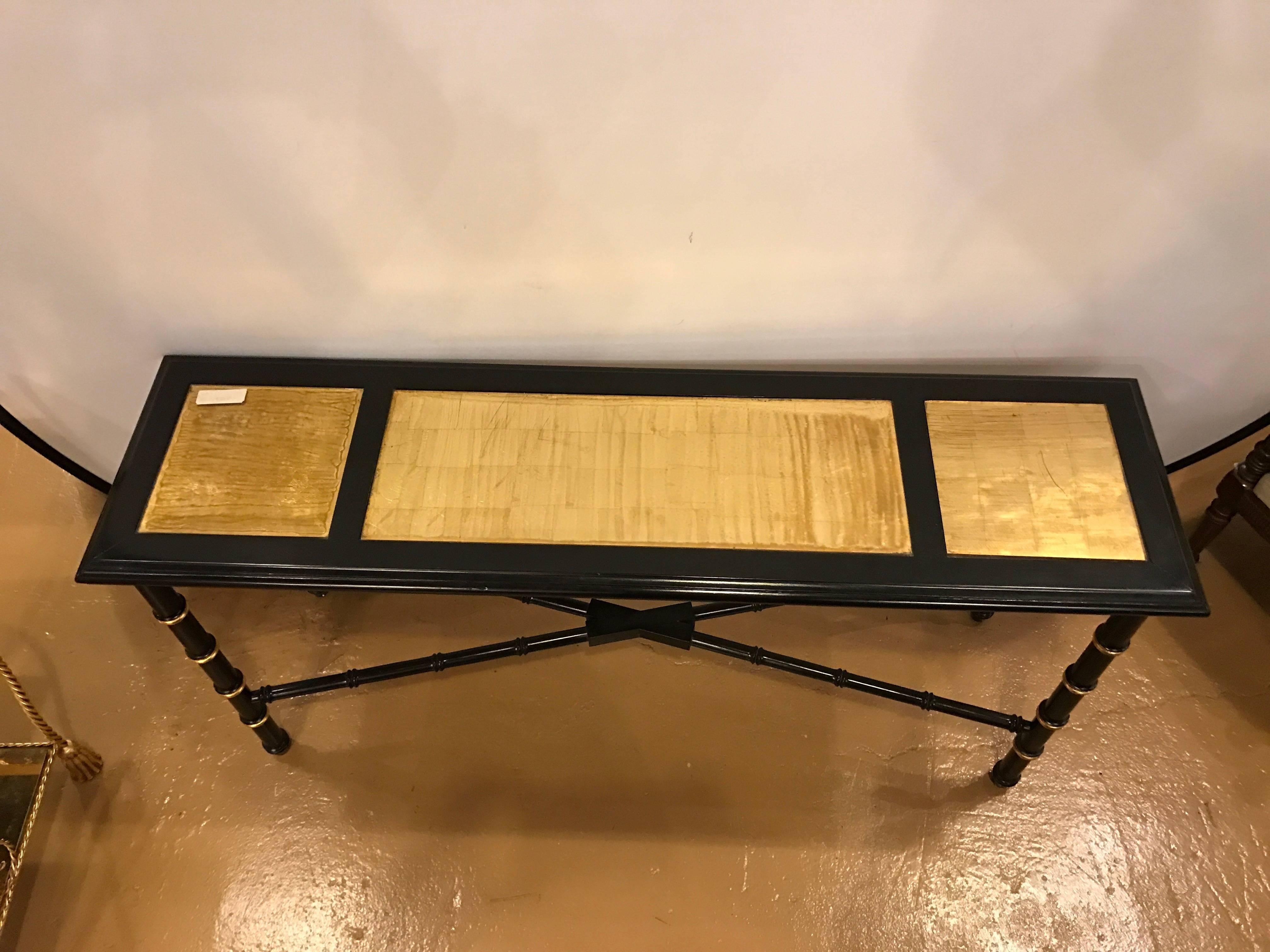 An ebonized faux bamboo and gilt gold console or serving table. The group of three gilt gold glass panels framed with ebony wood. The top supported by a group of faux bamboo and gilt gold legs held together by a faux bamboo X-shaped undercarriage.