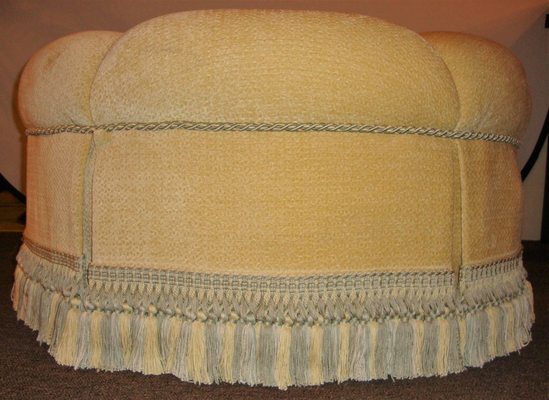 A circular finely upholstered and Lined ottoman with a tassel fringe base. Hollywood Regency at its finest.