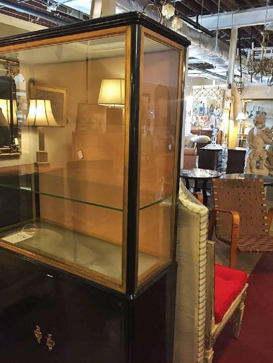 Hollywood Regency at its finest. Ebonized Louis XV Style China cabinet vitrine bookcase in the style of Maison Jansen. This bonze mounted bookcase or vitrine has a lower double door case supporting a vitrine shelved cabinet. The top appears to be