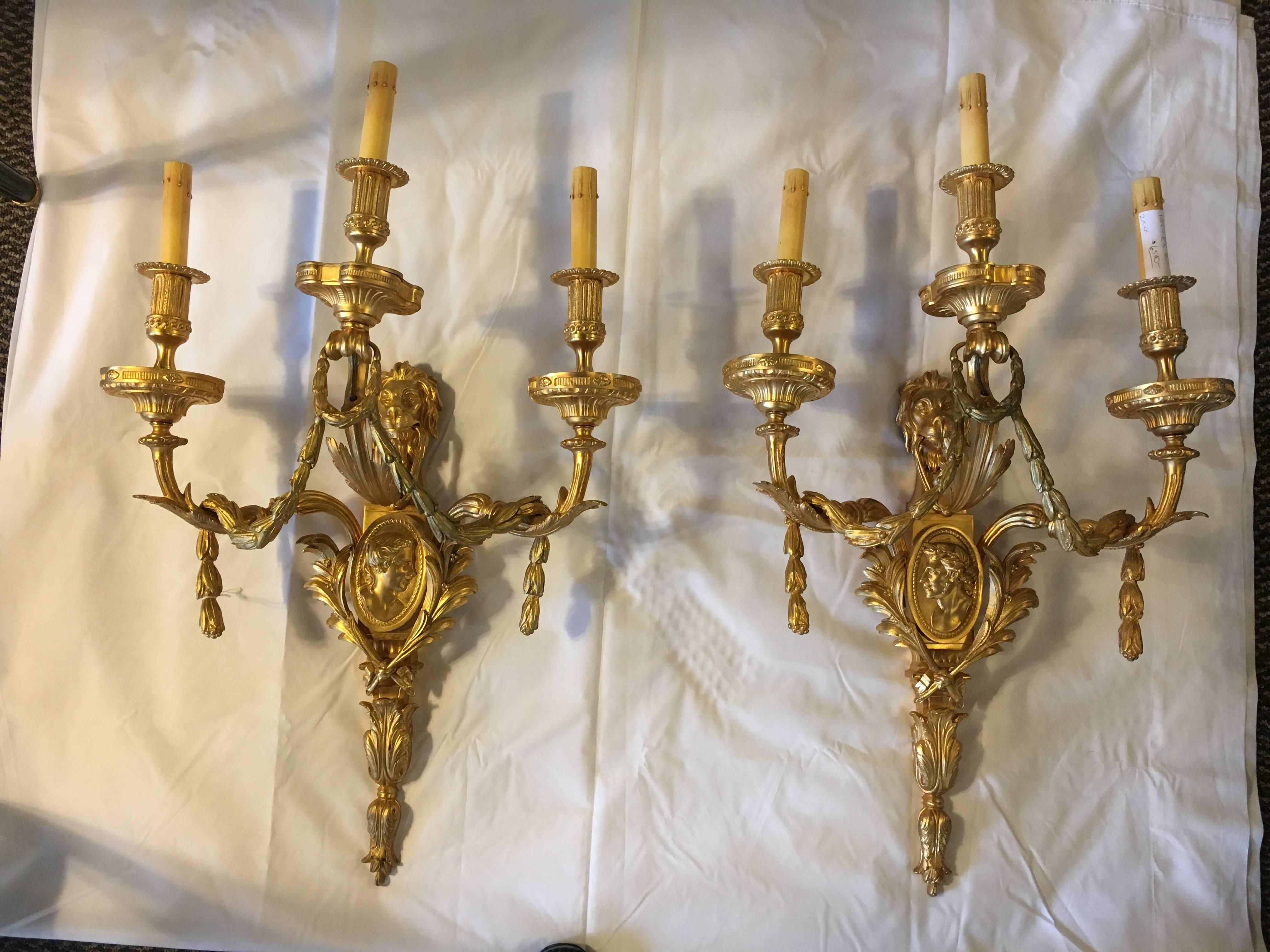 Pair of neoclassical style gilt bronze sconces. In the Louis XVI fashion these fine pair of detailed wall sconce each have three lights. Both with recent wiring. The pair with opposing male and female busts and adorning lion masks. Solid bronze.