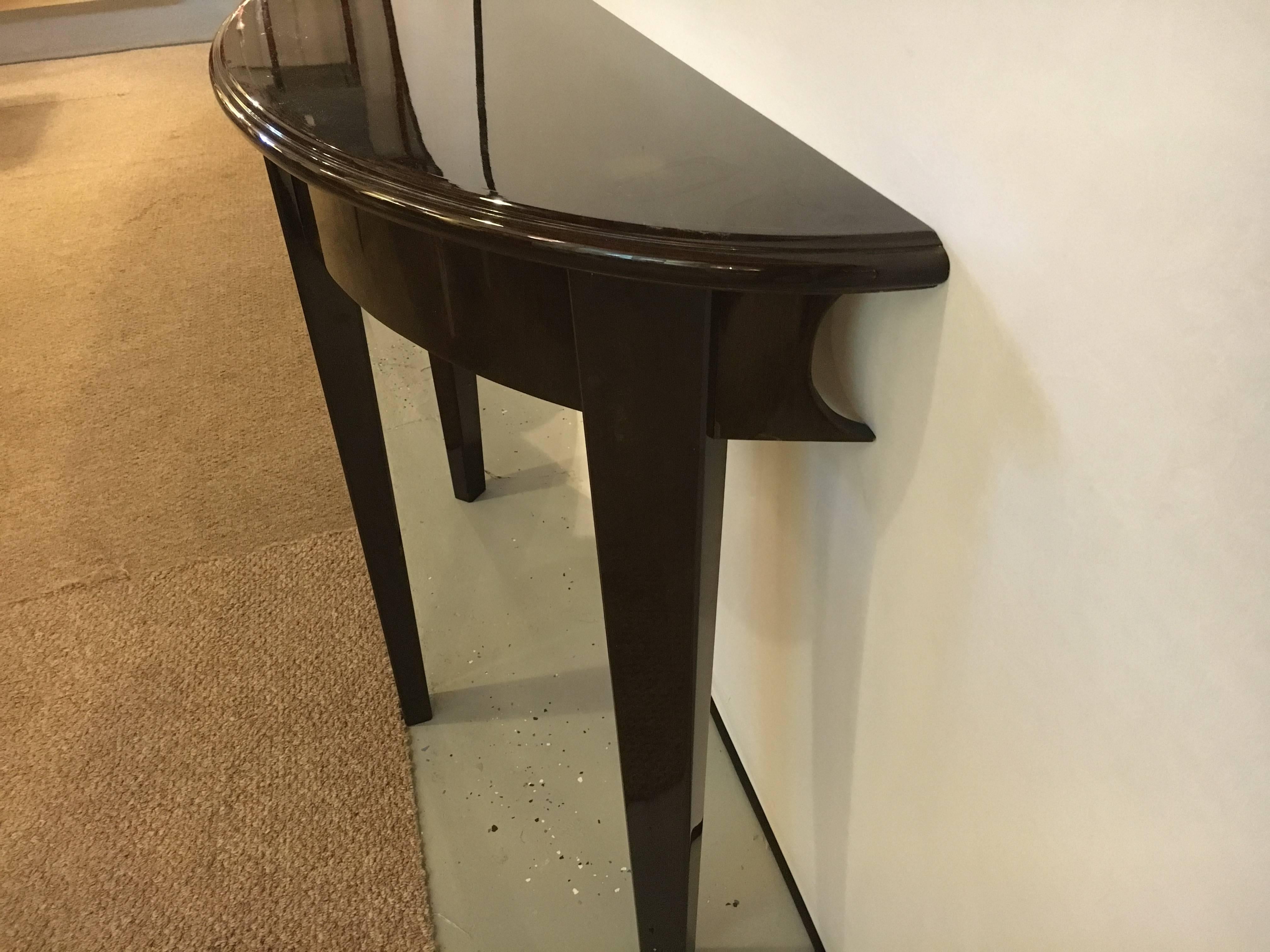 A pair of Hollywood Regency ebony mahogany demilune console tables. Each freestanding console having three tapering legs supporting a fine hi polished demilune tabletop with inverted u designed sides. This pair a copy of a fine pair by Tommi