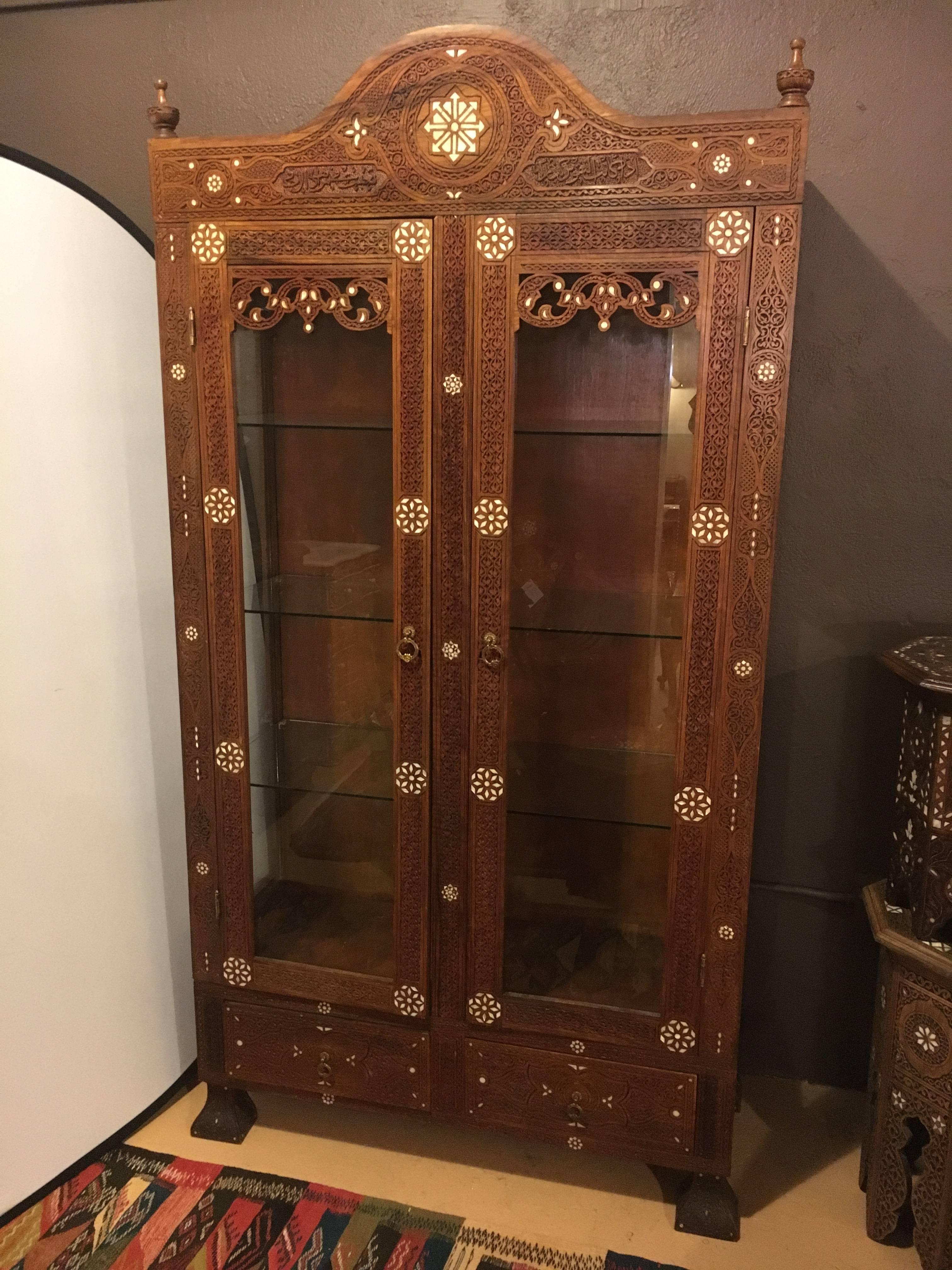 Antique Syrian cabinet hand-carved with mother-of-pearl inlays fine mid-19th century design. The bracket feet supporting a double glass door pair of finely inlaid mother-of-pearl doors with drawer bottom beneath.

 