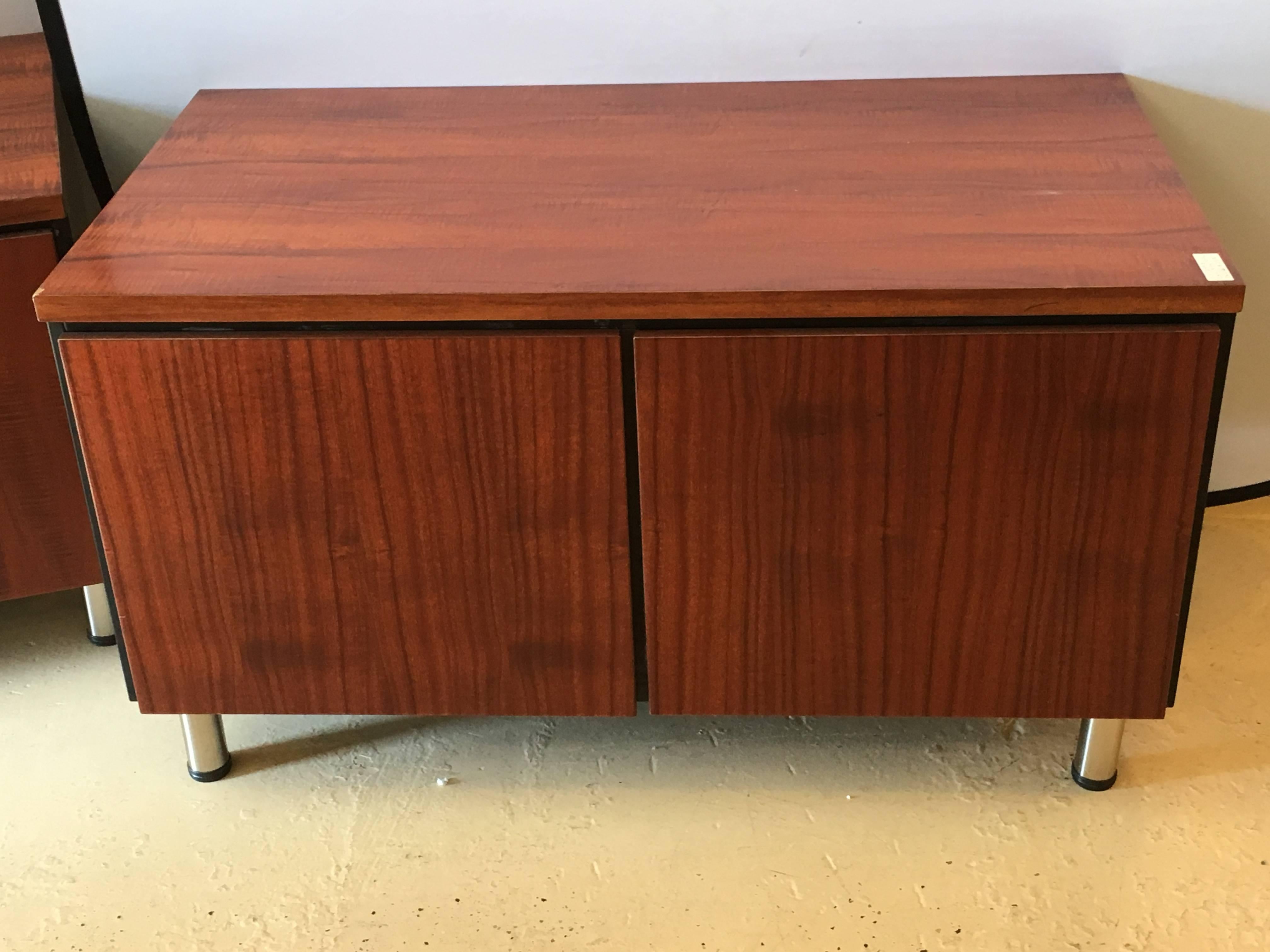 A pair of Mid-Century Modern rosewood with chrome feet chests. Adjustable shelf interior. The fronts having cylindrical chrome feet with black capped bottoms supporting two large door fronts leading to four open compartments of ebony wood. Each