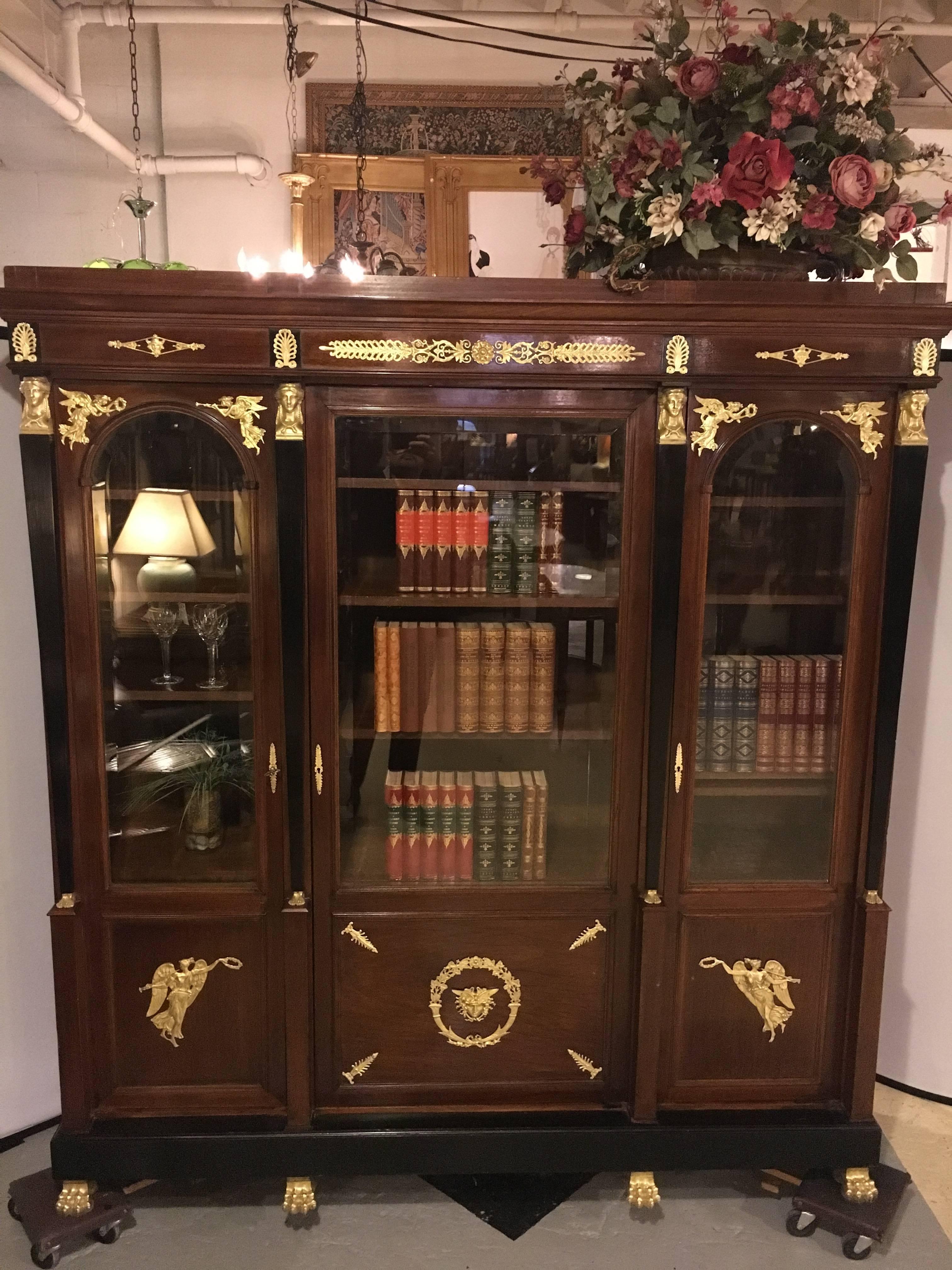 19th century Empire crotch mahogany doré bronze-mounted bookcase breakfront. Sitting on bronze claw feet stands this large and impressive antique bookcase. The over the top bronze mounts of the finest quality in doré'. Having a centre door of