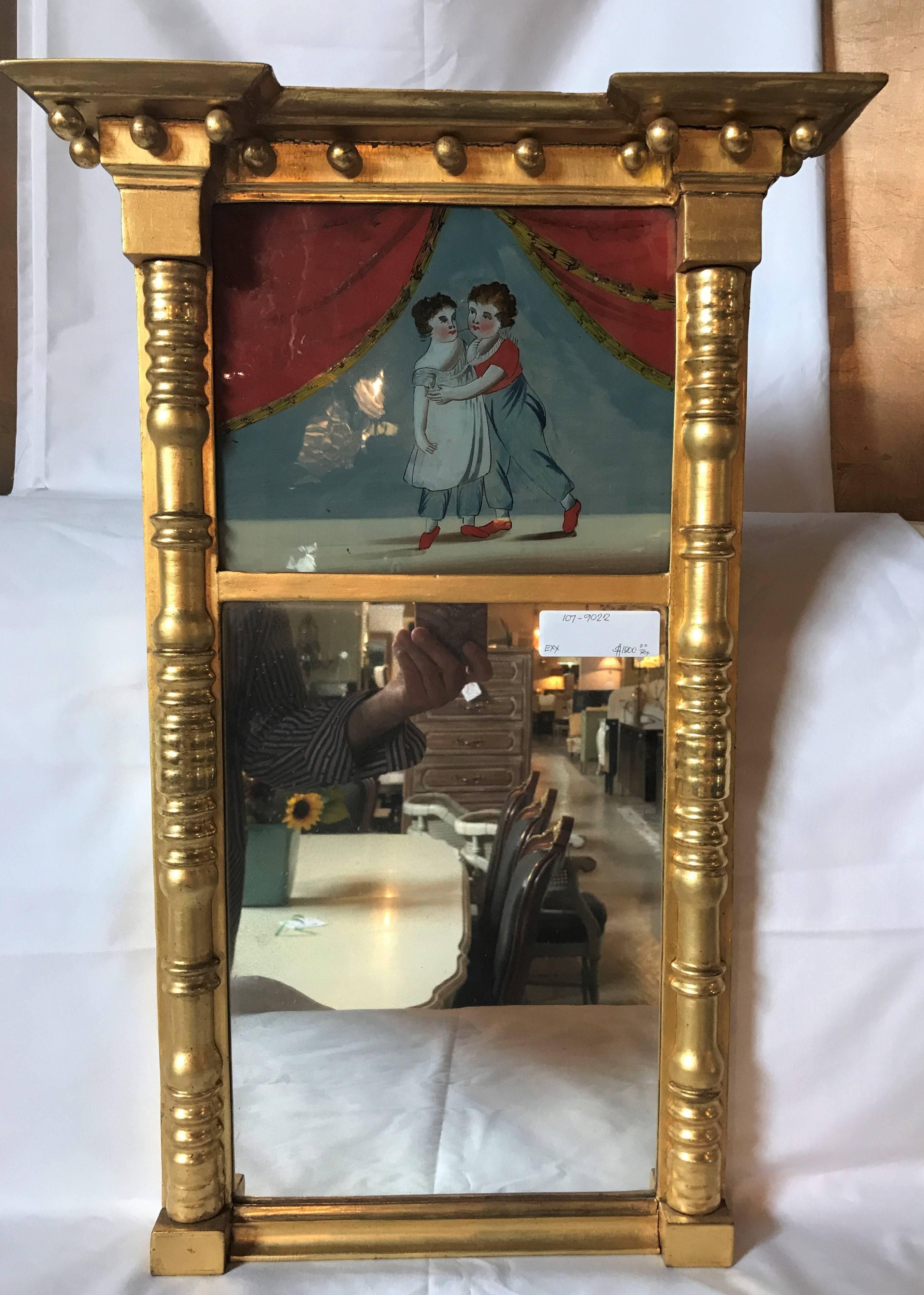 A simply stunning and sweet 19th century Federal guild gold framed wall mirror. This finely gilt wall mirror has a reverse painting of two lovers dancing. The outer mirror frame of column-form sides terminating in circular ball form top.