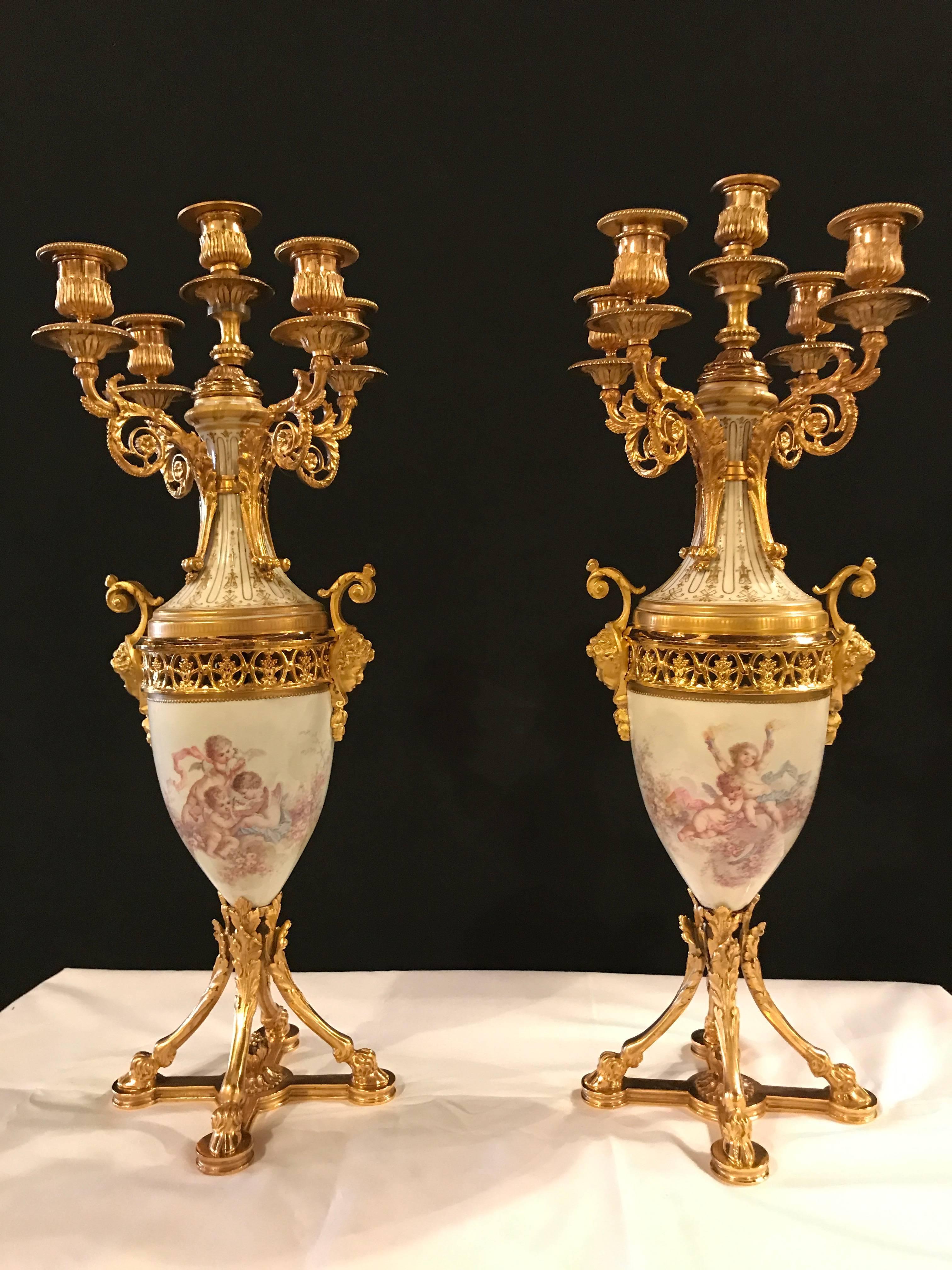 A fine pair of gilt bronze and porcelain candelabra with cherub painting. Each having five candleholders of bronze form with scrolling arms leading to a centre urn shaped porcelain paint of cherubs playing with love birds. The urns sitting on a four