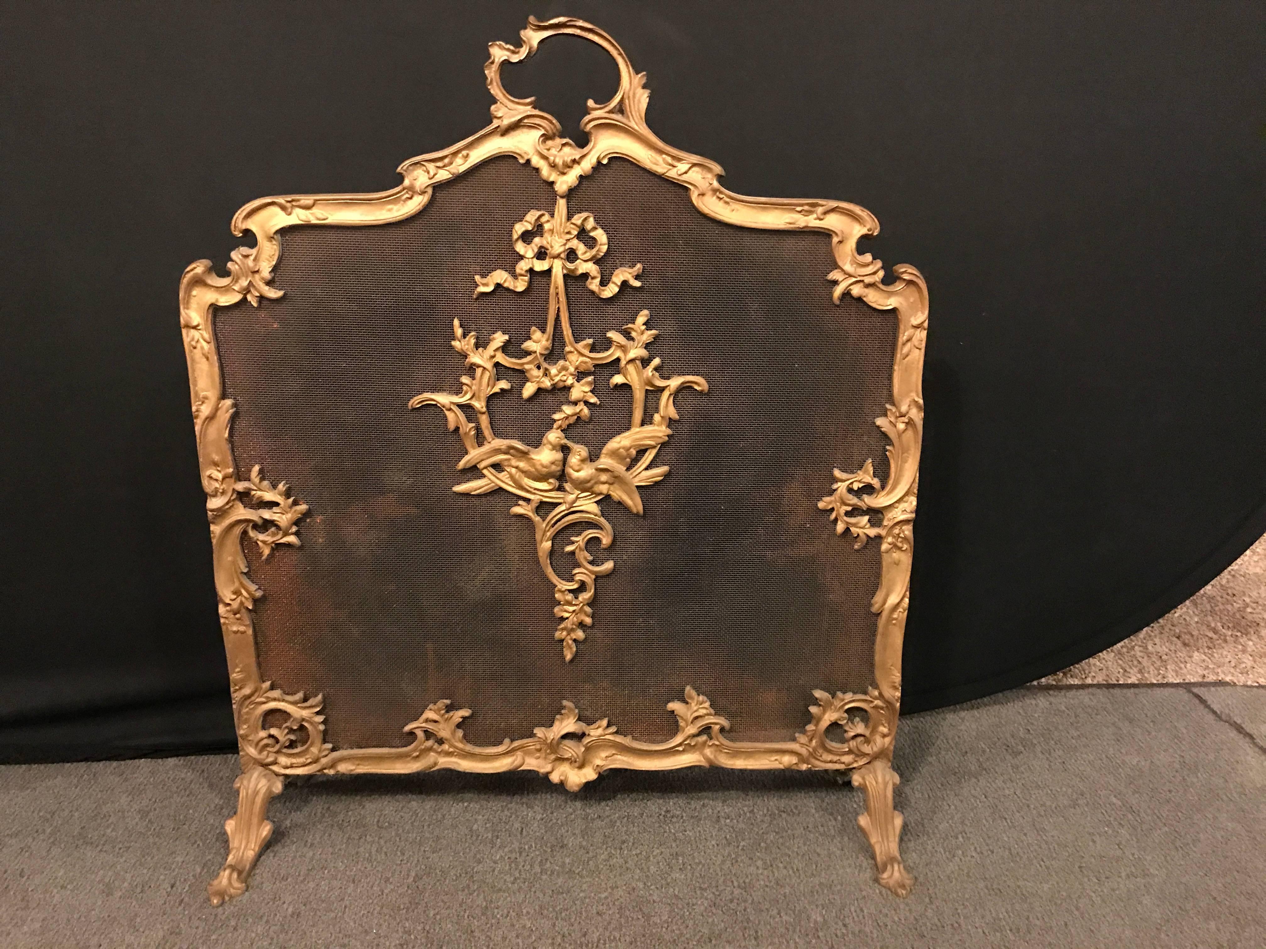 A Louis XV style French bronze fire screen. Sitting on claw feet is this bronze framed fire screen in the Louis XV manner. The center depicting a pair of love birds under a bow and wreath. Finely cast in a doré bronze re-gilded finish. lXAX.
