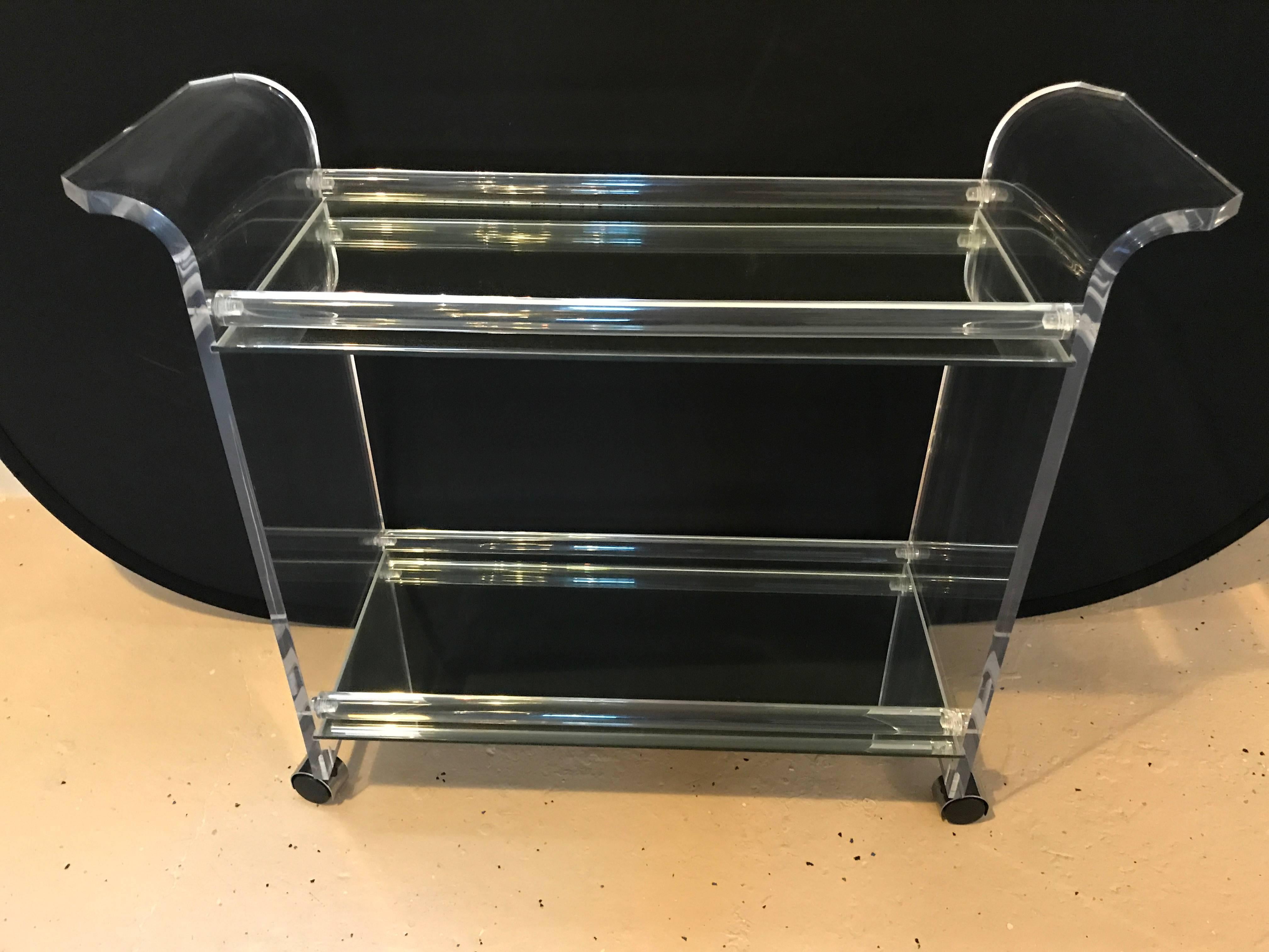 Two-Tier Lucite and mirror rolling bar cart or serving table. This highly functional cart sits on casters which glide easily across the floor with a lower and upper mirrored top shelf supporting by curved thick Lucite sides.