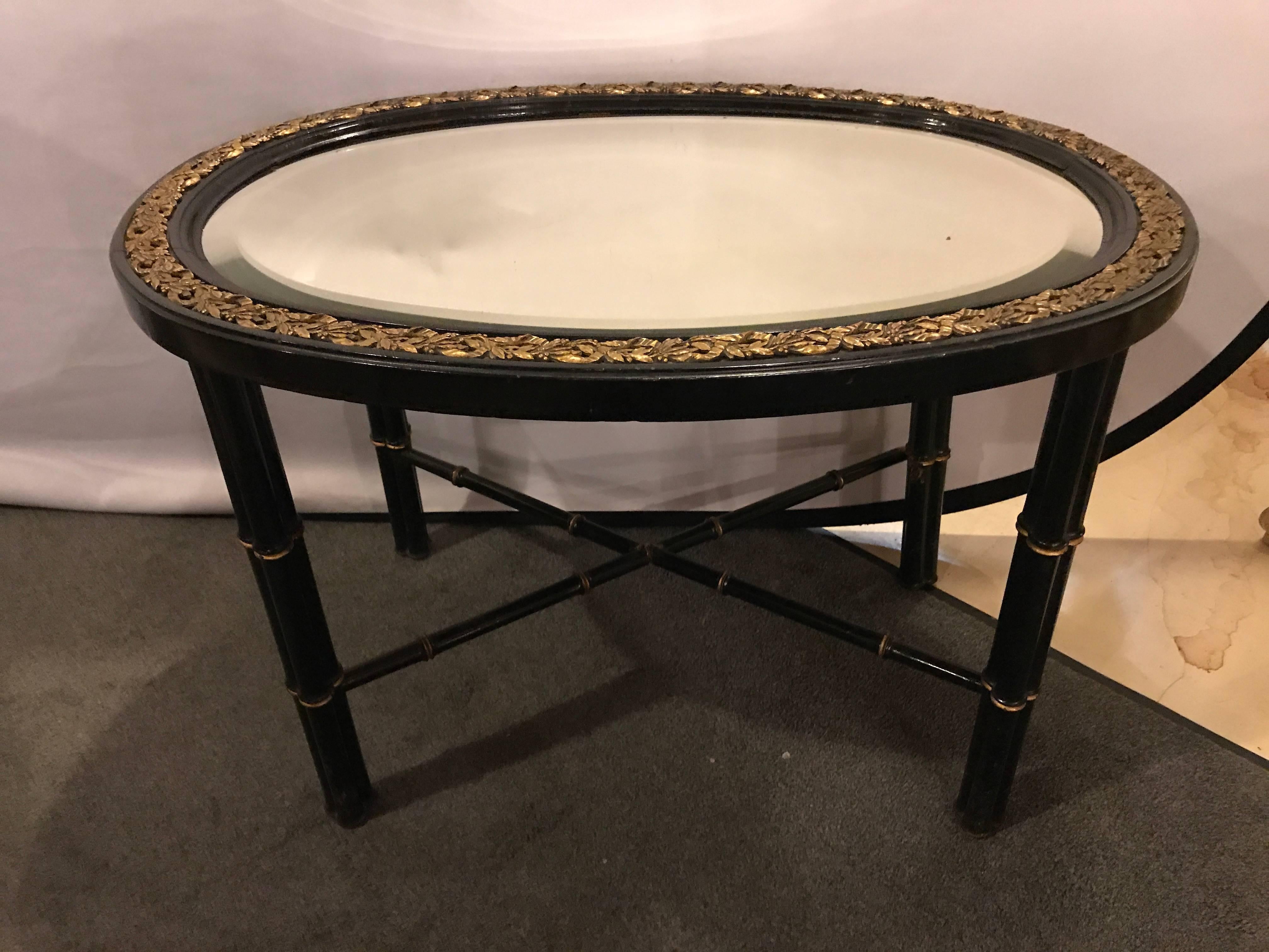 Beveled mirror top black oval coffee table with bronze mounts. This fine Hollywood Regency bamboo form coffee table has a charm and allure that is certain to bring attention to itself. The beveled mirror oval top having a bronze framed border of