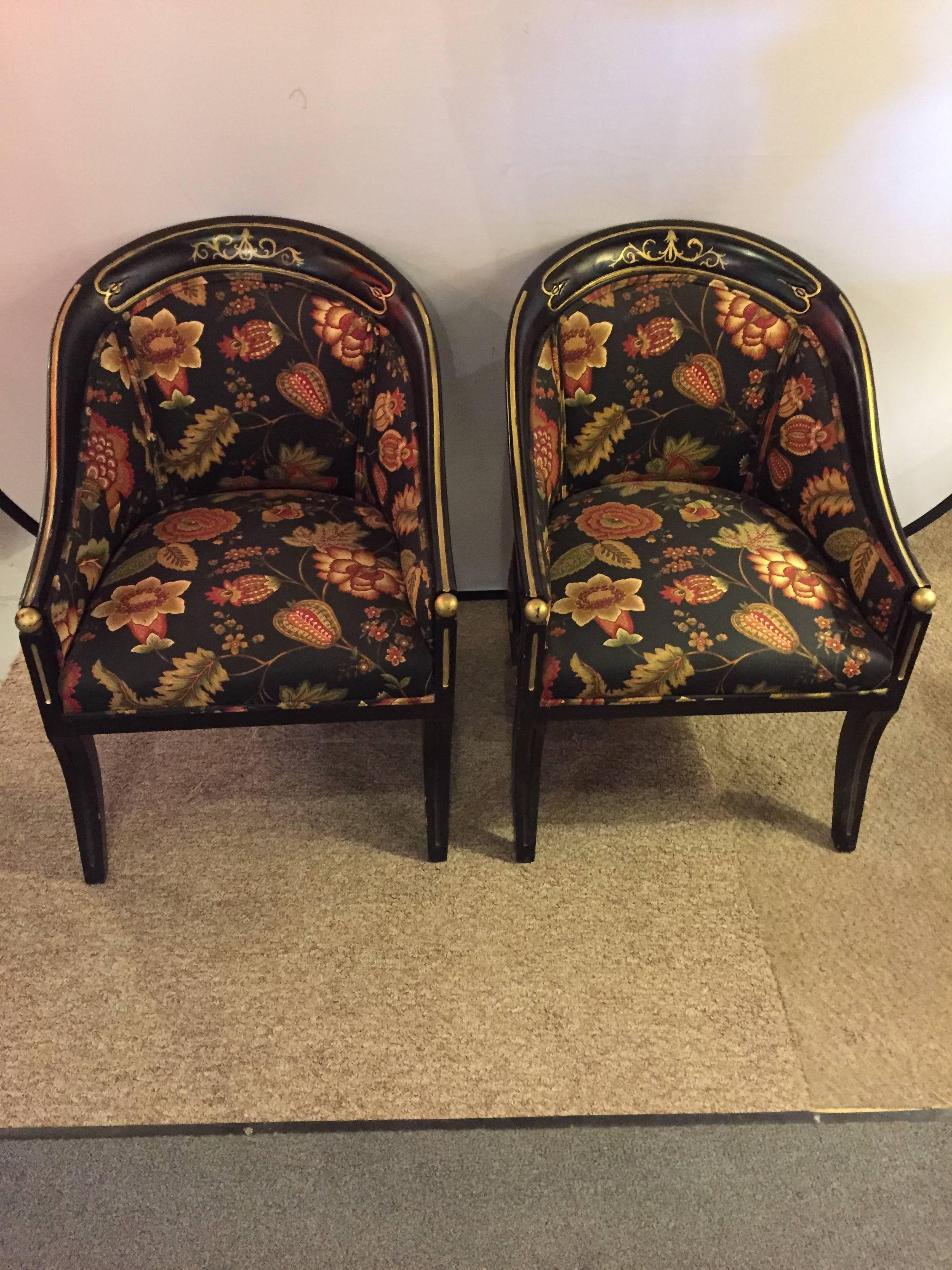 A pair of Hollywood Regency style ebonized armchairs. Each having an ebonized frame with side arms having gilt gold decorated balls on the hand rests. Both with floral upholstery and gilt scroll and line design on the back and arms.