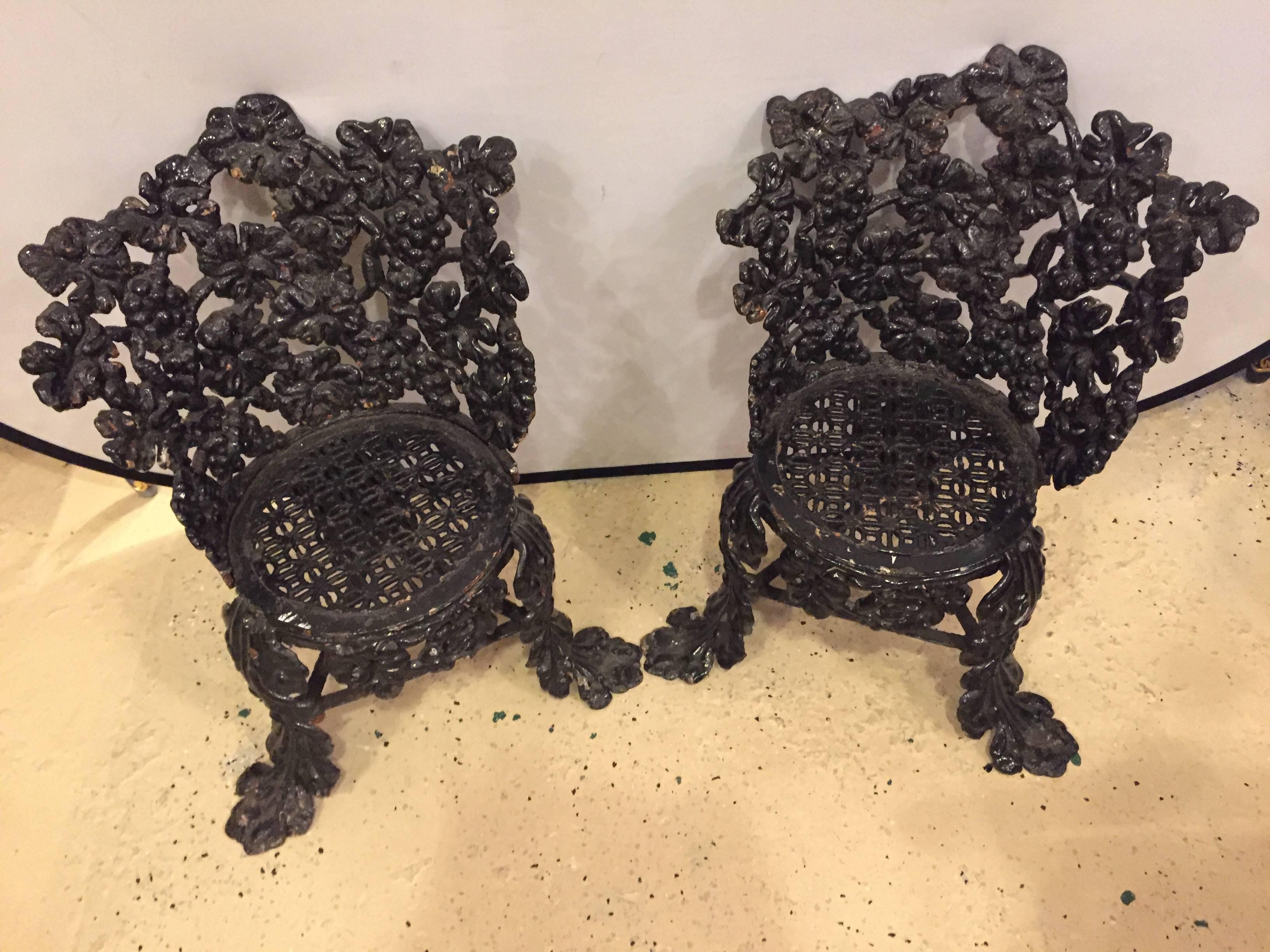 A pair of cast iron small garden chairs. Each having fruit design. Both painted black. Fine condition.