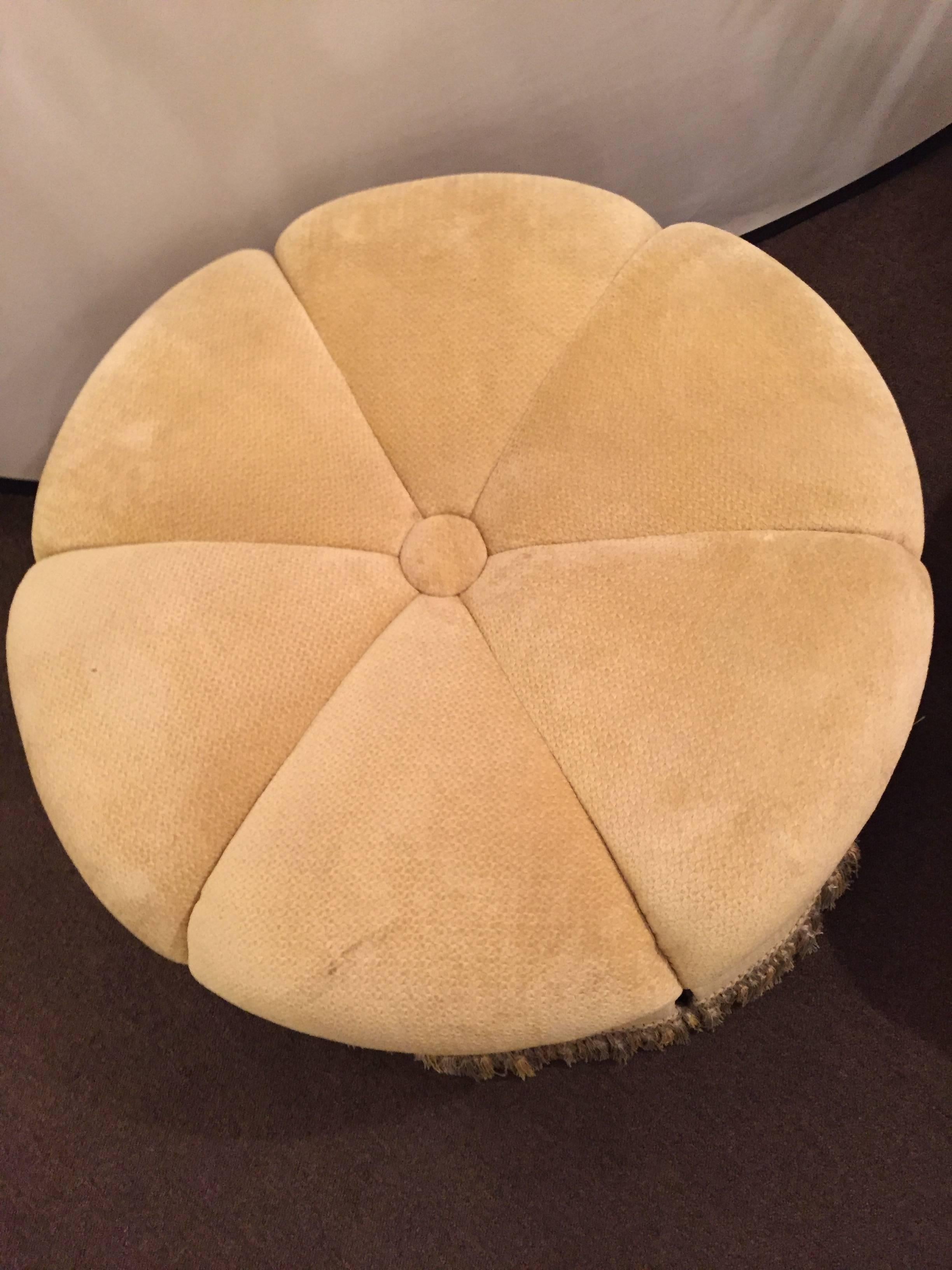 A circular finely upholstered and lined ottoman or pouf with a tassel fringe base. Done in the Hollywood Regency style this ottoman is finely detailed and very decorative.