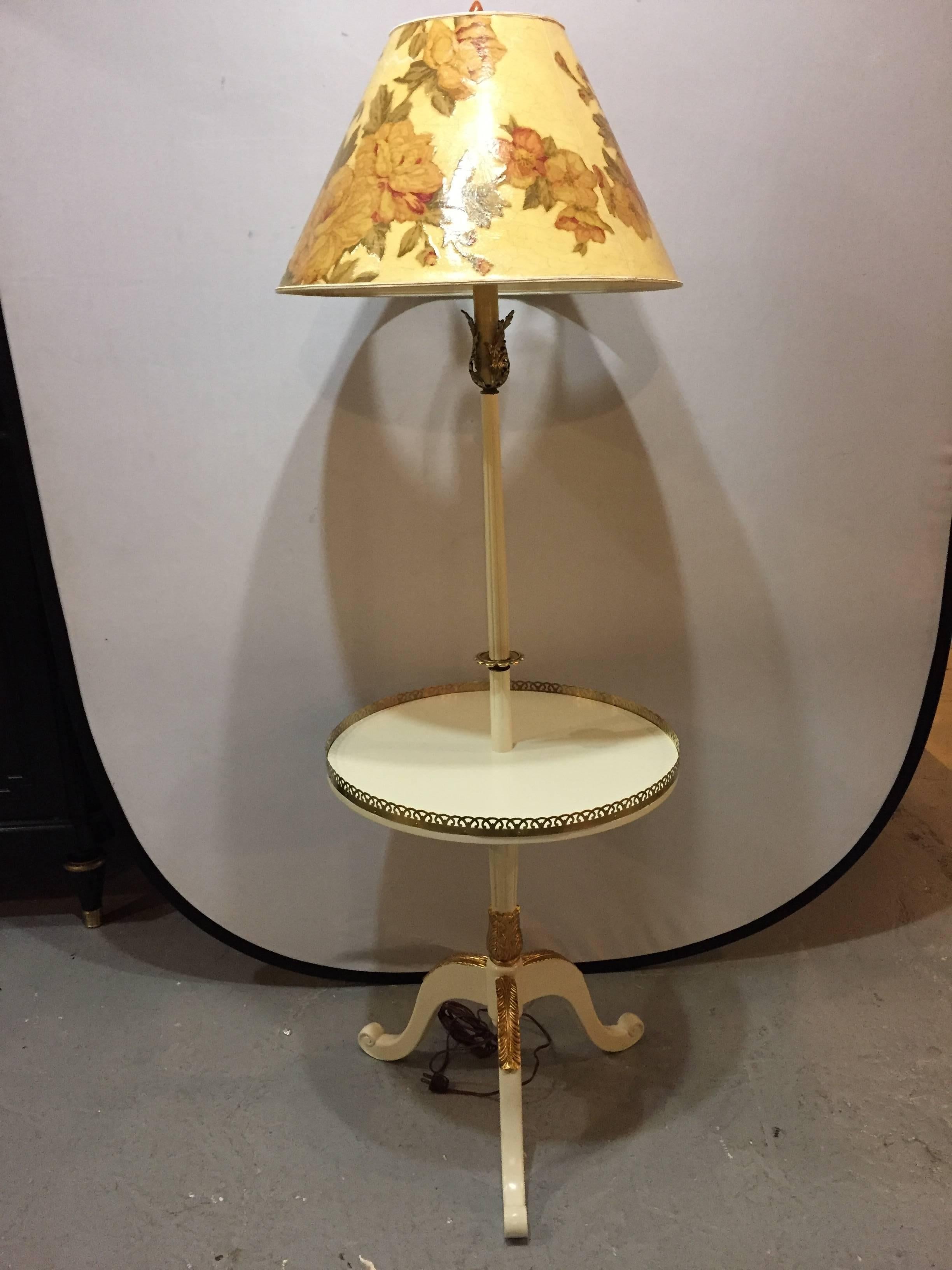 A off-white and gilt gold paint decorated table lamp with custom shade. Sitting on a tri-pod base with a center pedestal leading to a bronze galleried tabletop, this finely paint decelerated lamp would surely shine in any room in the home.