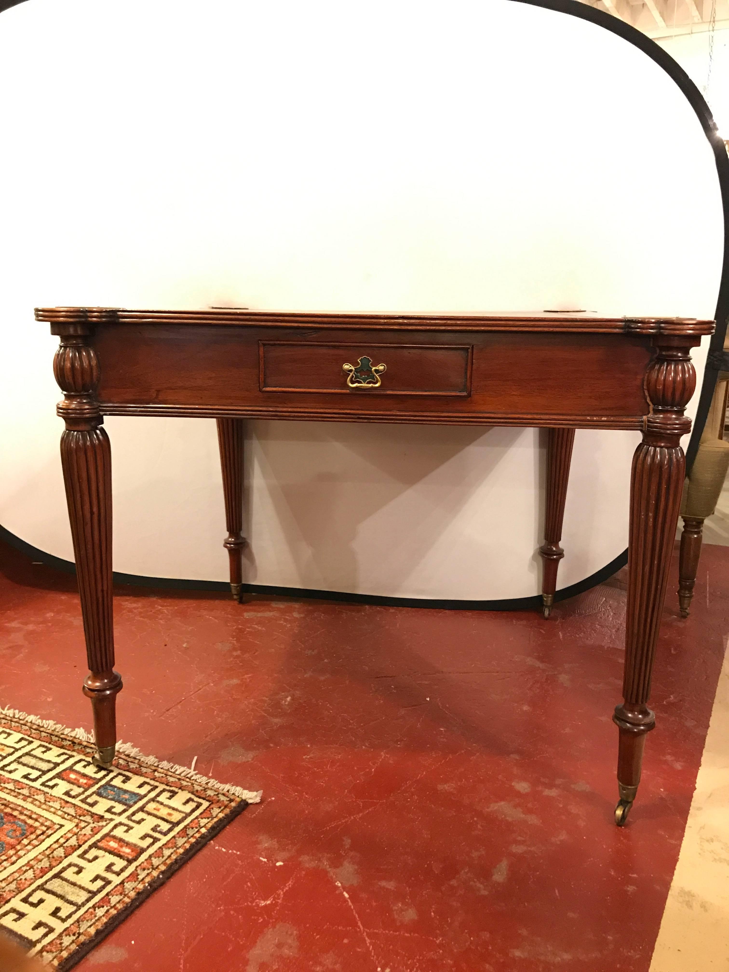 A leather top mahogany card table in the manner of Maitland Smith. This fine custom quality card table has a tooled leather top with gilt design flanked by four brass coin trays. The apron having four drawers to store each players personal items.
