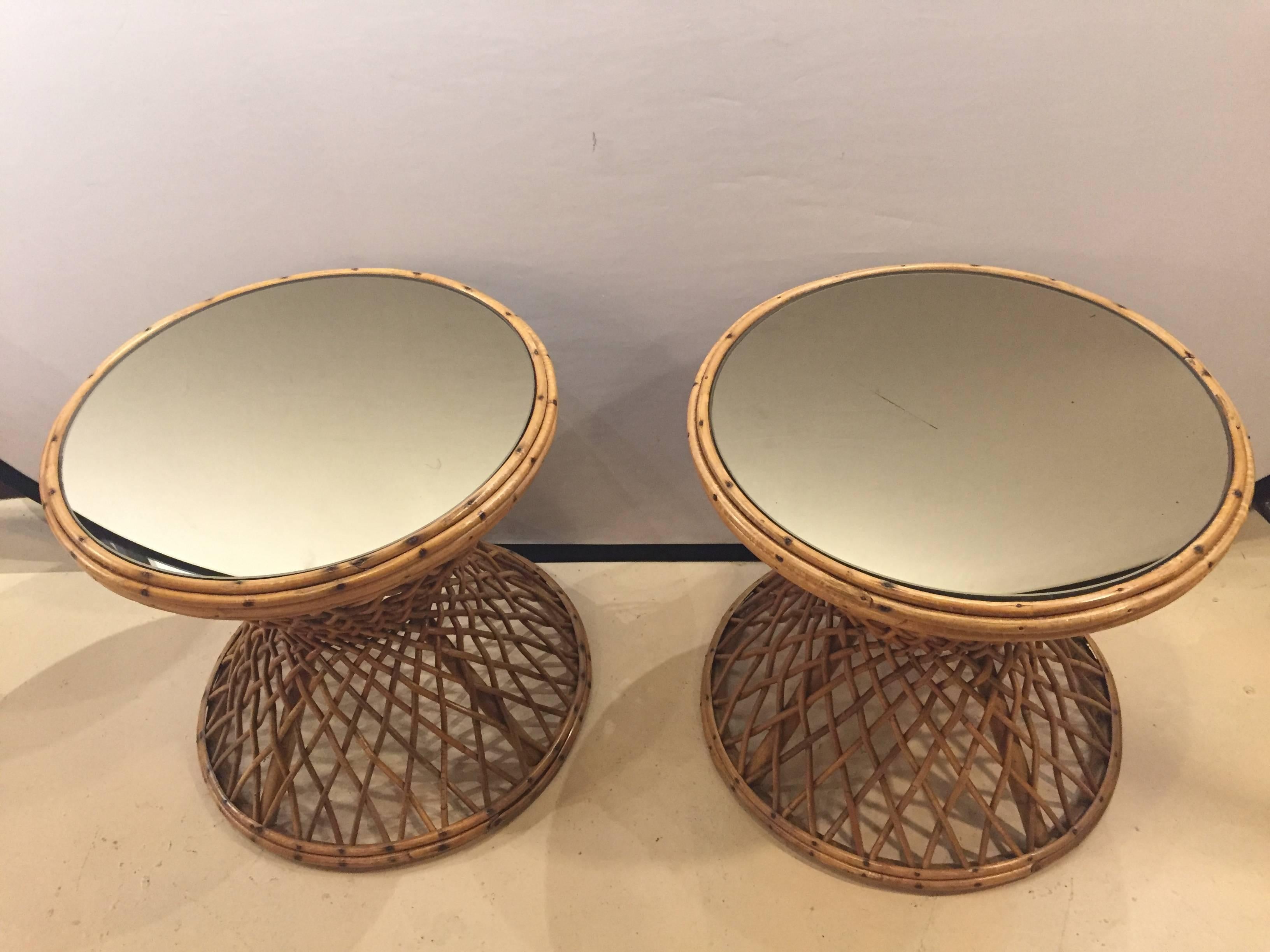 A pair of rattan mirrored top end tables. Each having a circular form rattan back of double column-form upper and lower tiers supporting a circular mirrored top. Can be used inside or outside. This pair sure to sparkle in any Florida room or seating