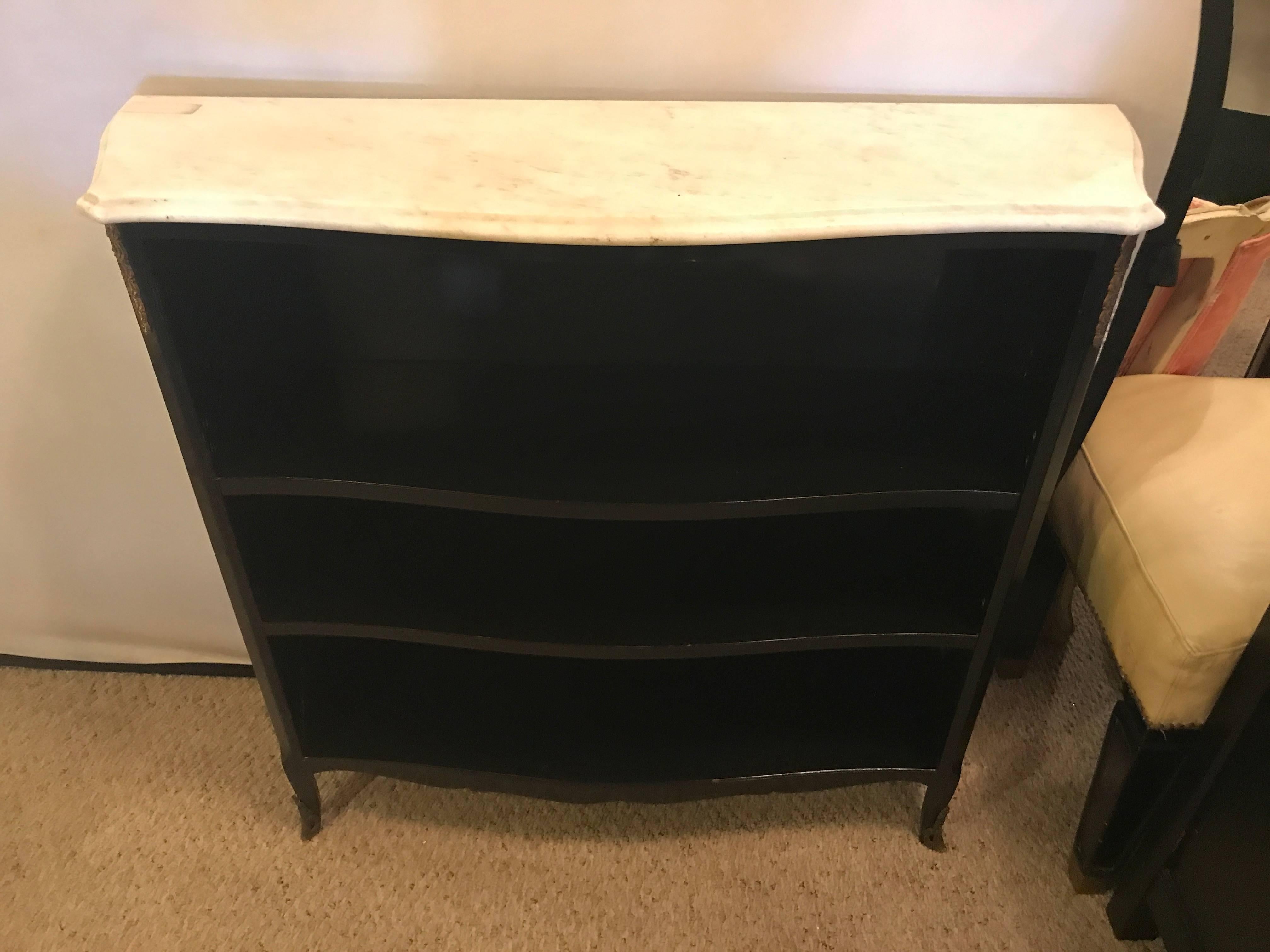 Hollywood Regency ebony marble-top bookcase or console table attributed to Maison Jansen. Having a white marble top supported by a case with three shelved areas for books. The corners and feet with bronze mounts.