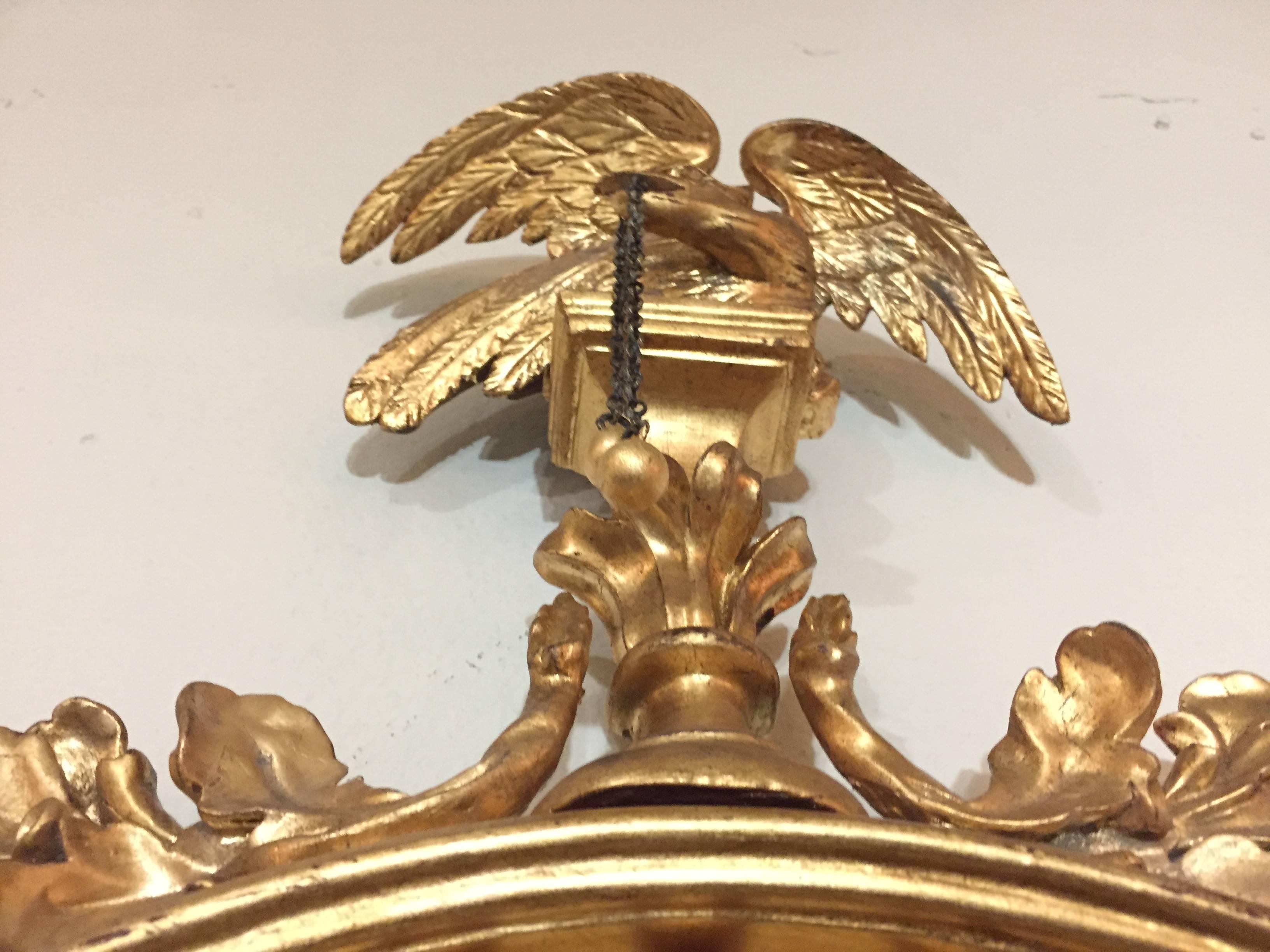 A late 19th or very early 20th century Federal style convex mirror ebony and gilt decorated adorning an eagle winged crest. This antique federal style wall or console mirror is detailed with the finest carvings. The top depicting a wonderfully