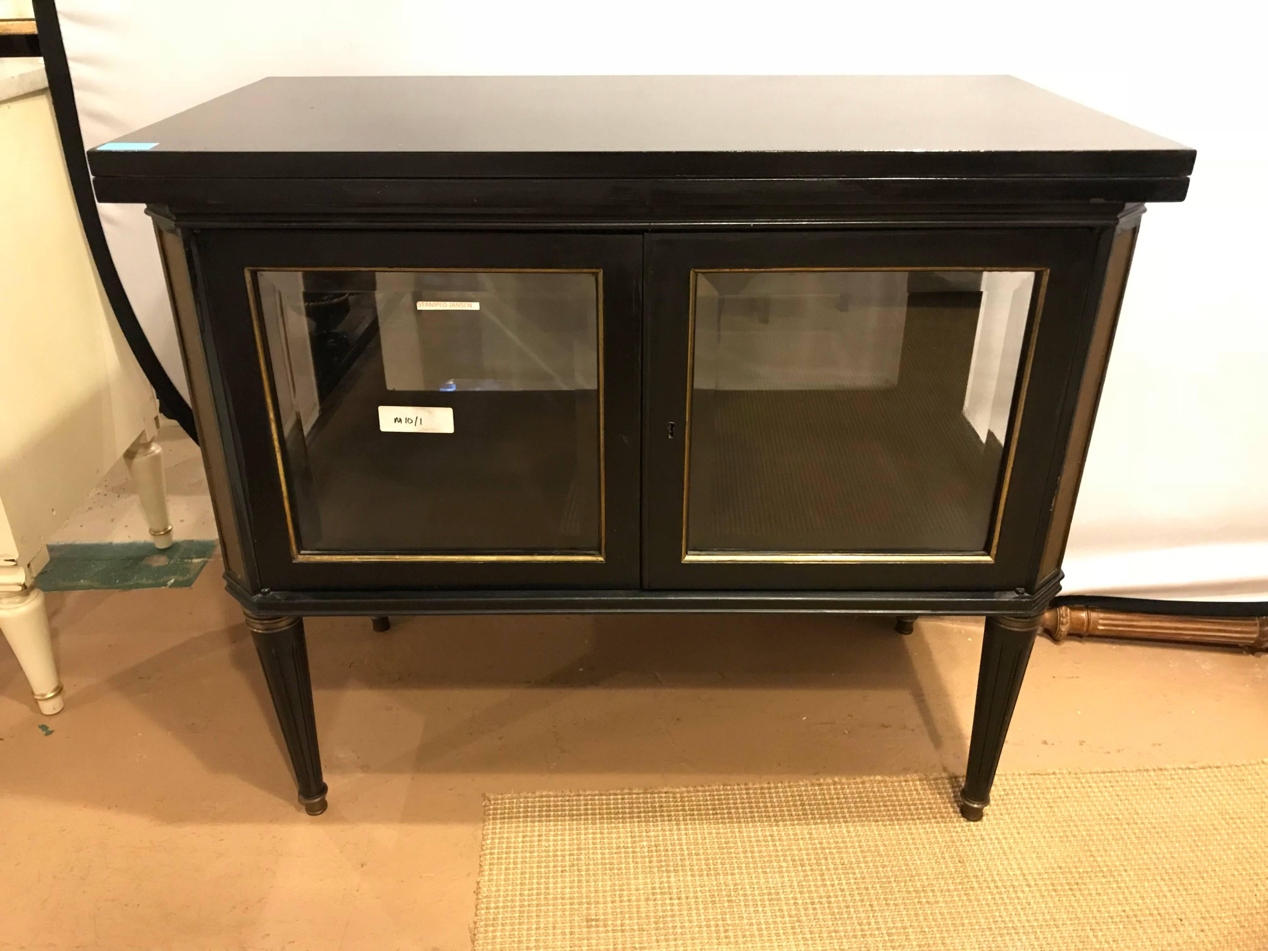 A Maison Jansen bronze-mounted Vitrine Server. This fine Hollywood Regency server has a flip-top that extends to a small dining table or server. The beveled glass front pair of doors with beveled sides display a vitrine or bar cart setting. The