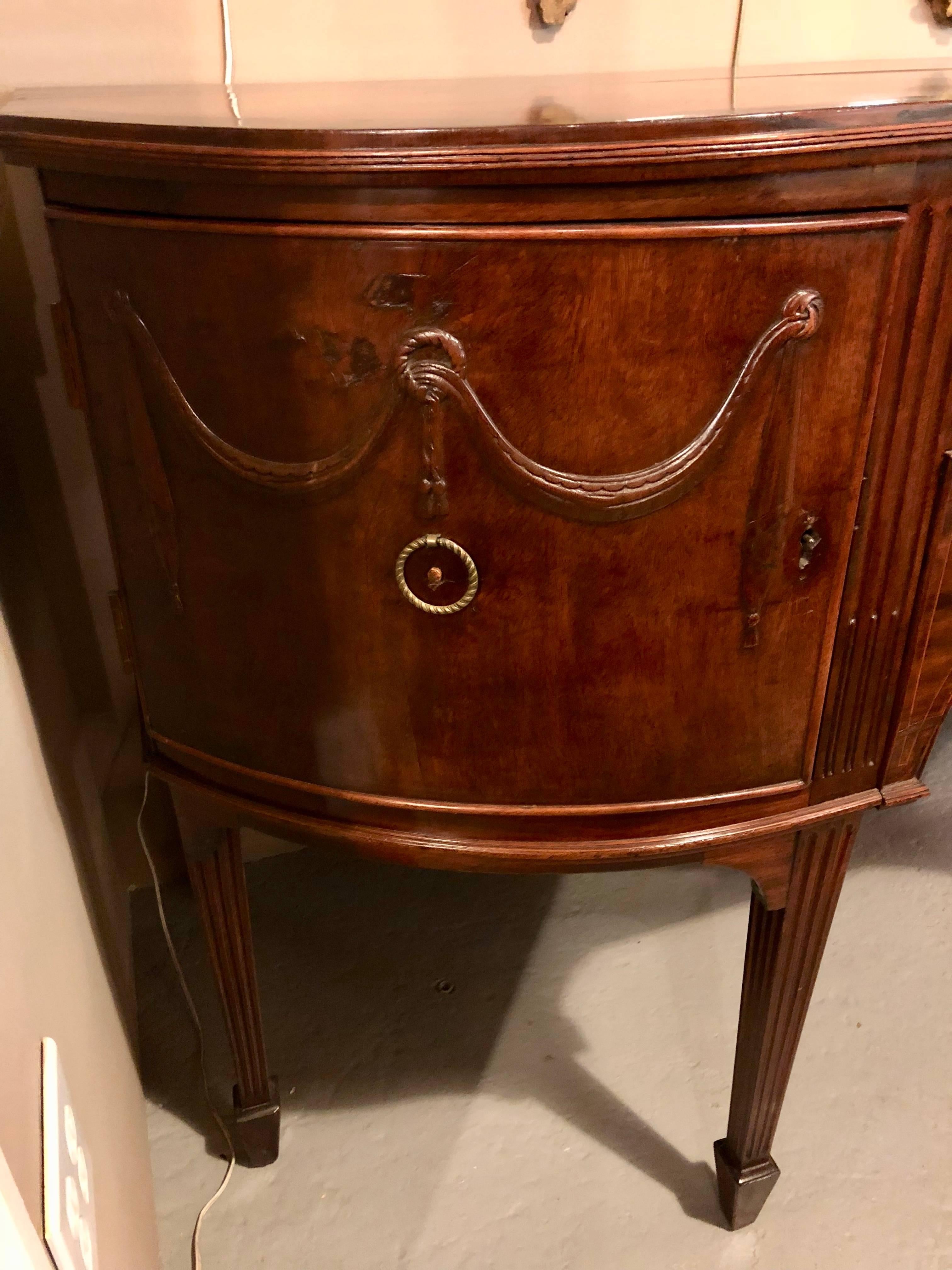 A Georgian period demilune sideboard or serving table breakfront. This 18th-early 19th century sideboard has fine proportions as well as fine intricate carvings. The spade feet leading to tapering legs supporting an upper case of two center drawers,