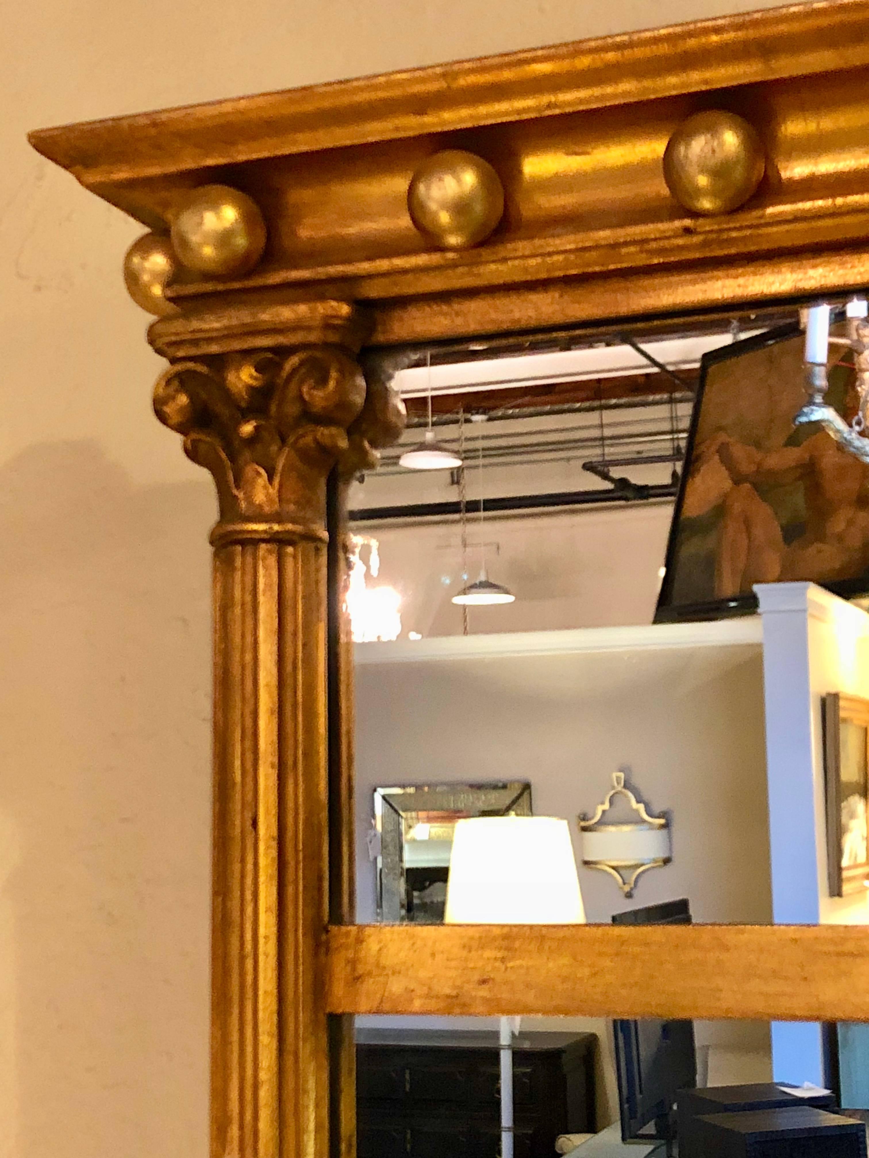 Pair of gilt gold wall or console mirrors with column-form sides and carved tops. A pair of custom quality Hollywood Regency pair of mirrors that are certain to make any room or setting shine.