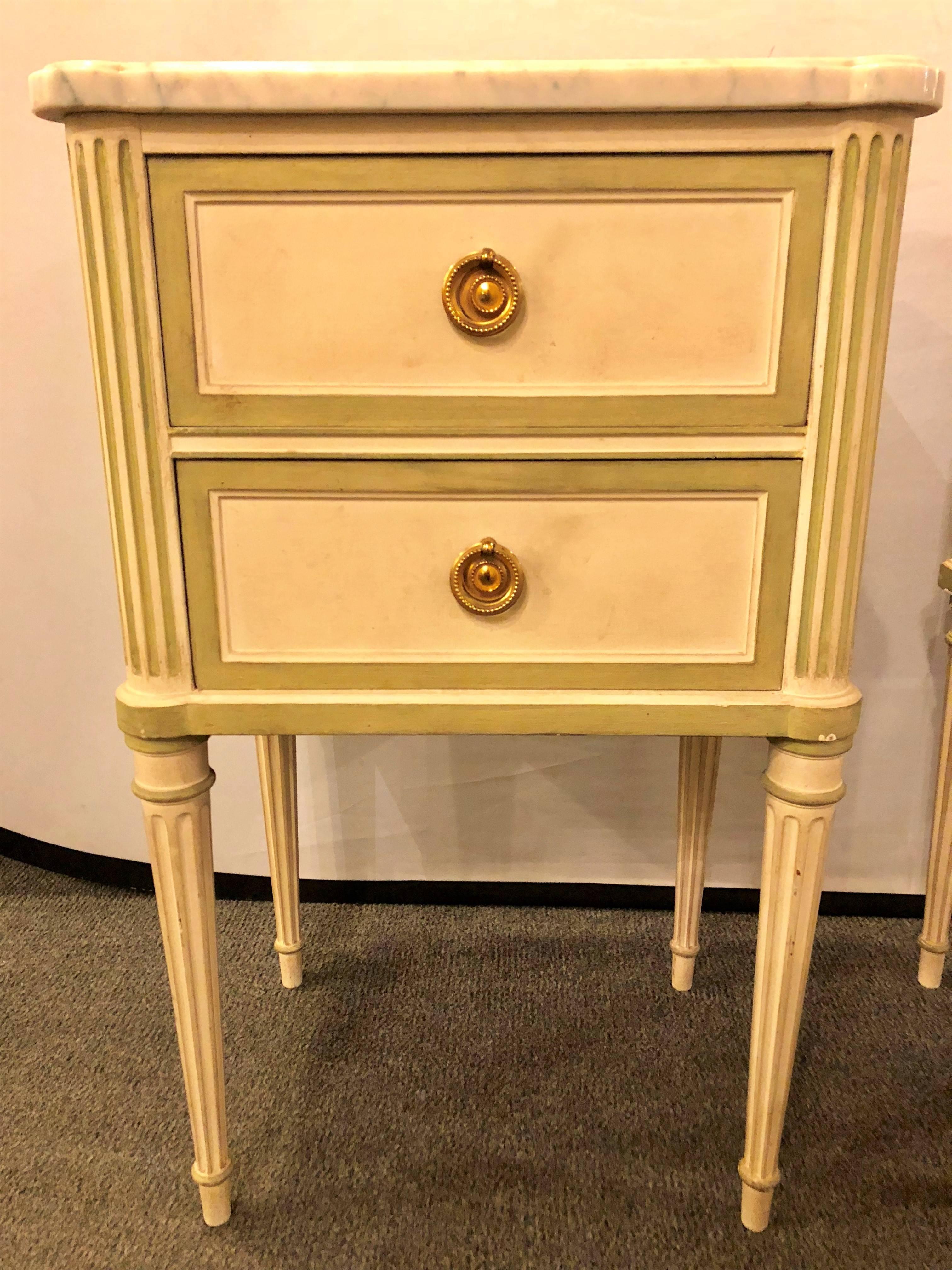 Pair of Louis XVI style paint decorated marble top end tables or nightstands. This pair of custom quality distressed and aged stands each having a white marble top on an olive green decorated frame with a linen white background. Having two drawers