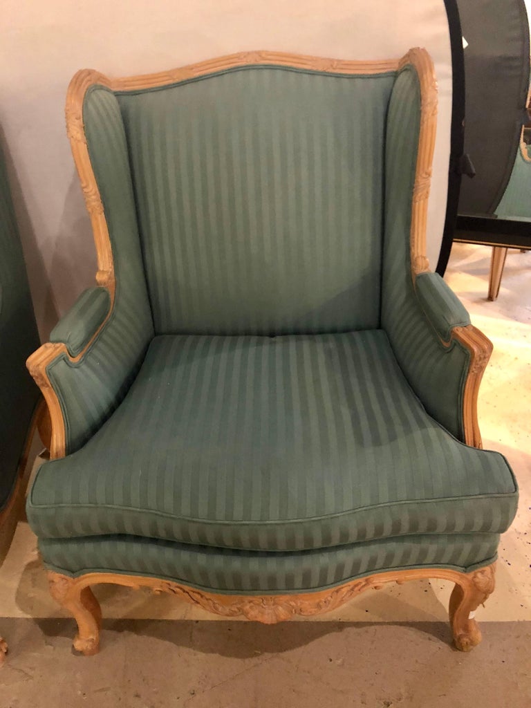 A pair of Louis XV style high back lounge or wing chairs. This pair of finely carved solid wooden Lounge Chairs would make a statement in any Living room or Office setting. The greenish stripped upholstery is clean and with very minor tatter. The