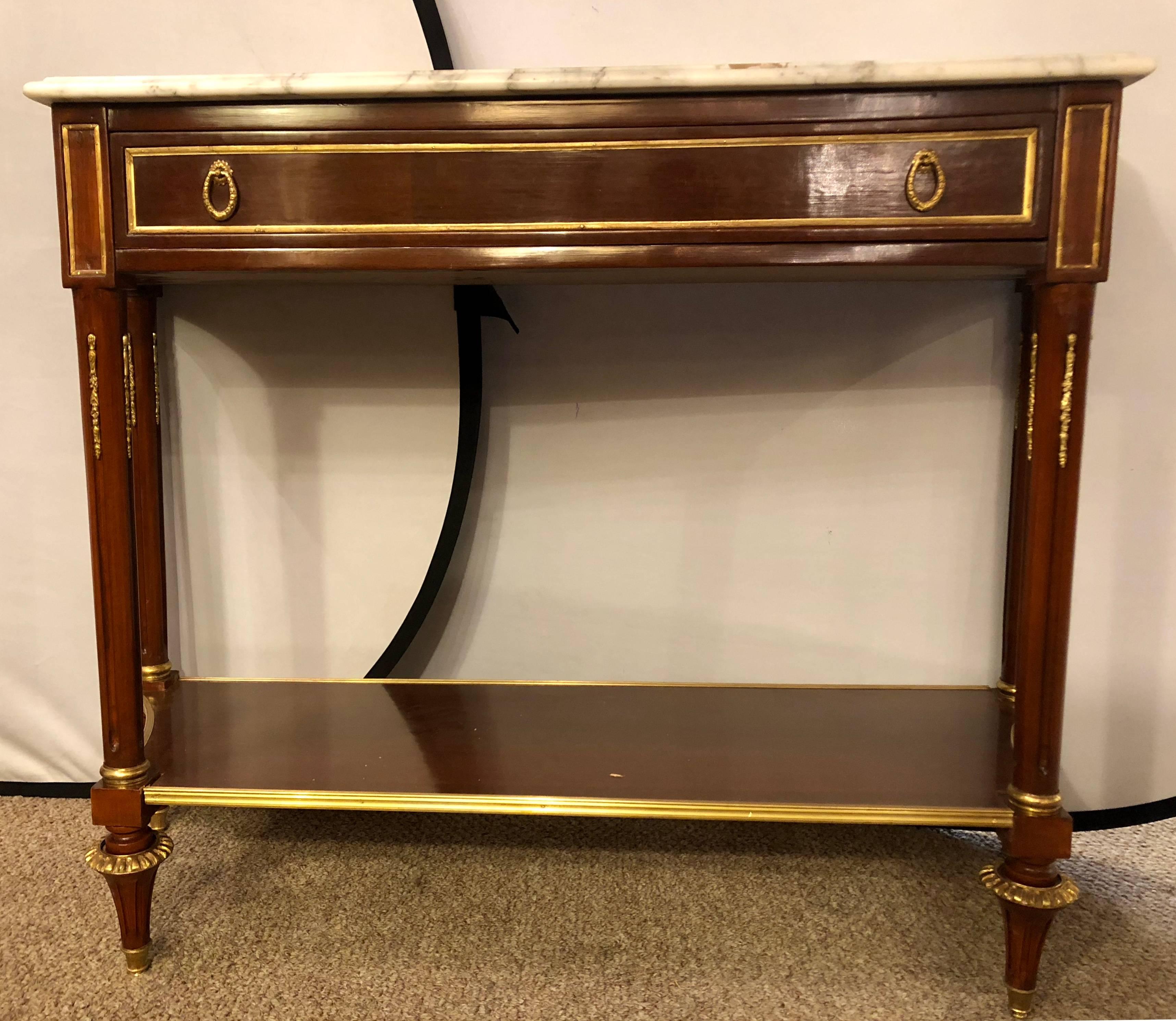 Pair of mahogany marble-top consoles with inverted sides and bronze framed lower shelves. This fine pair of custom quality Jansen inspired console tables in the Russian neoclassical manner have a lower shelf with bronze framing supported by a set of